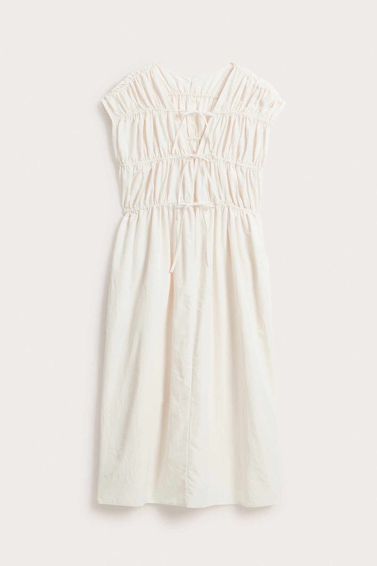 Forfra, hvit polyester-maxikjole med rynket overdel og to justerbare knytedetaljer.