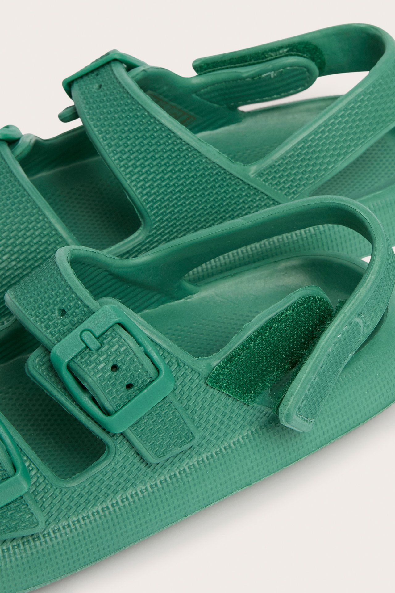Närbild av gröna plastsandaler med texturerade remmar, spänne och kardborreknäppning.