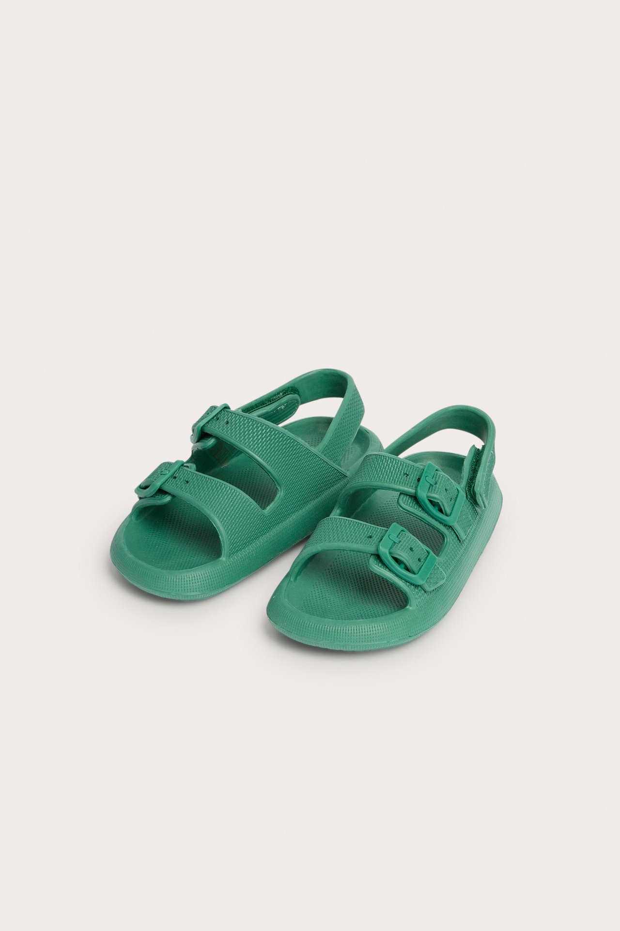 Framifrån: gröna plastbarnsandaler med justerbara remmar och spännen.