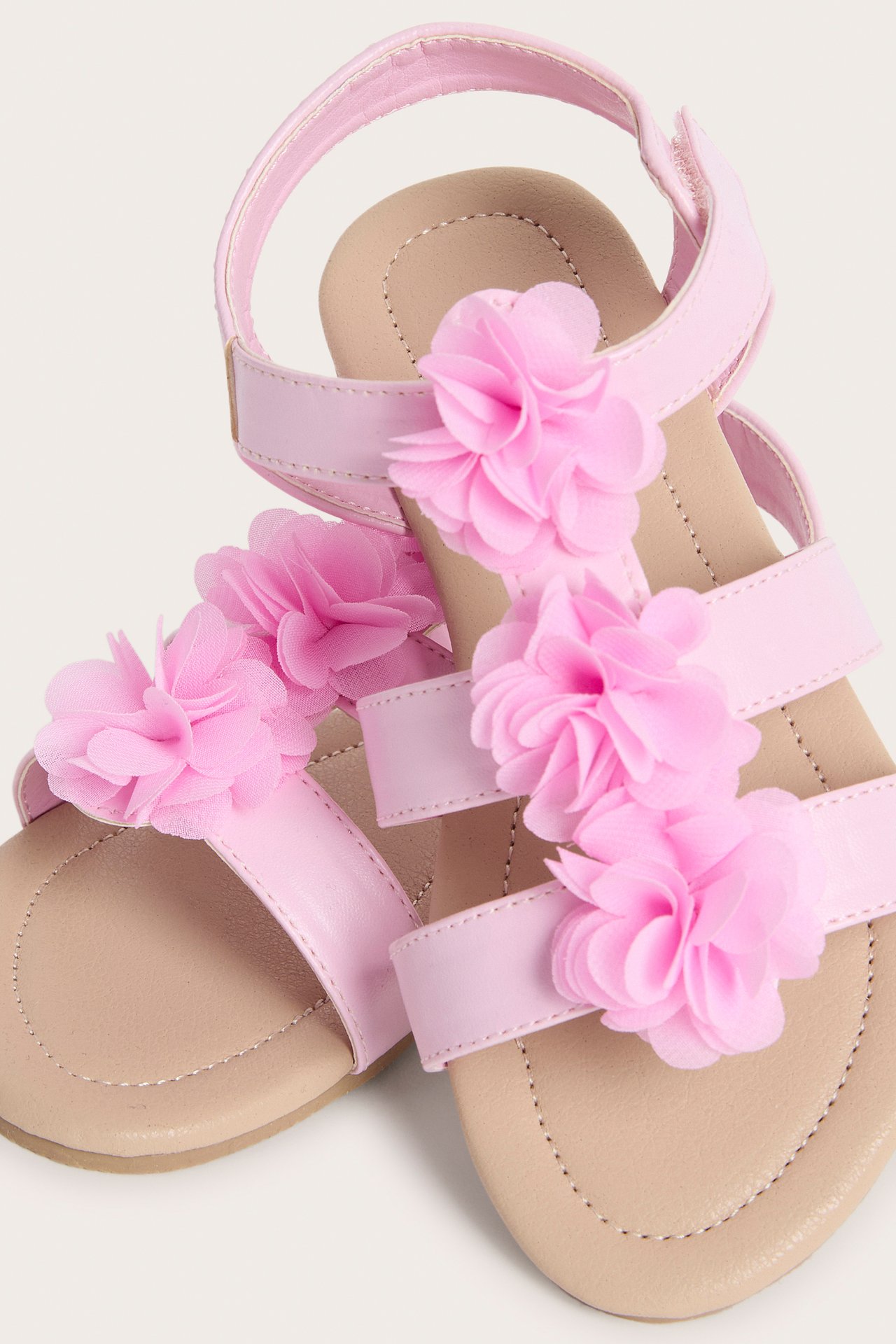 Närbild av rosa sandaler för barn med tygblommor och kardborreknäppning på ankelremmen.