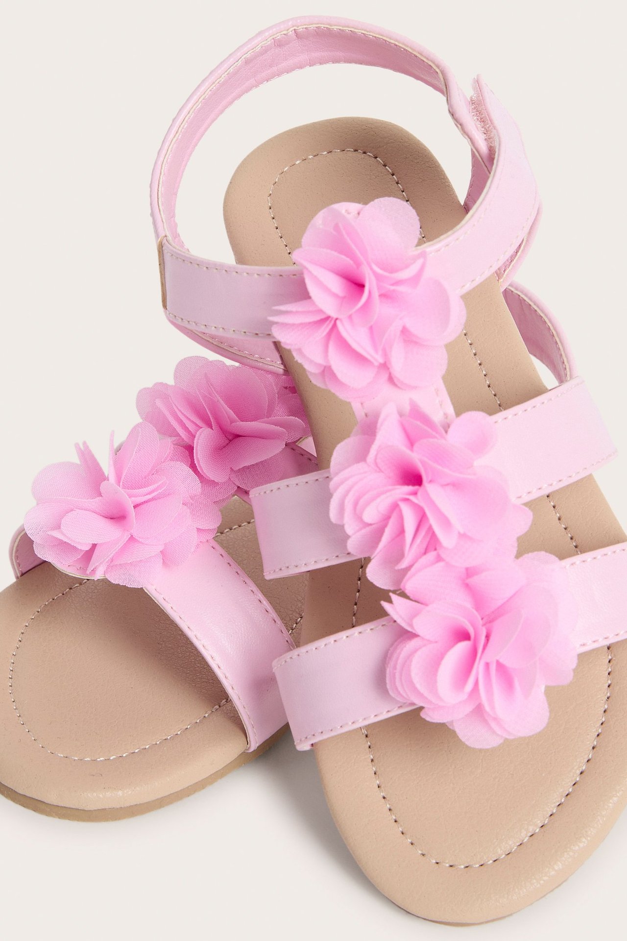 Zbliżenie na różowe sandały dziecięce z aplikacjami z kwiatów materiałowych i zapięciem na rzep.