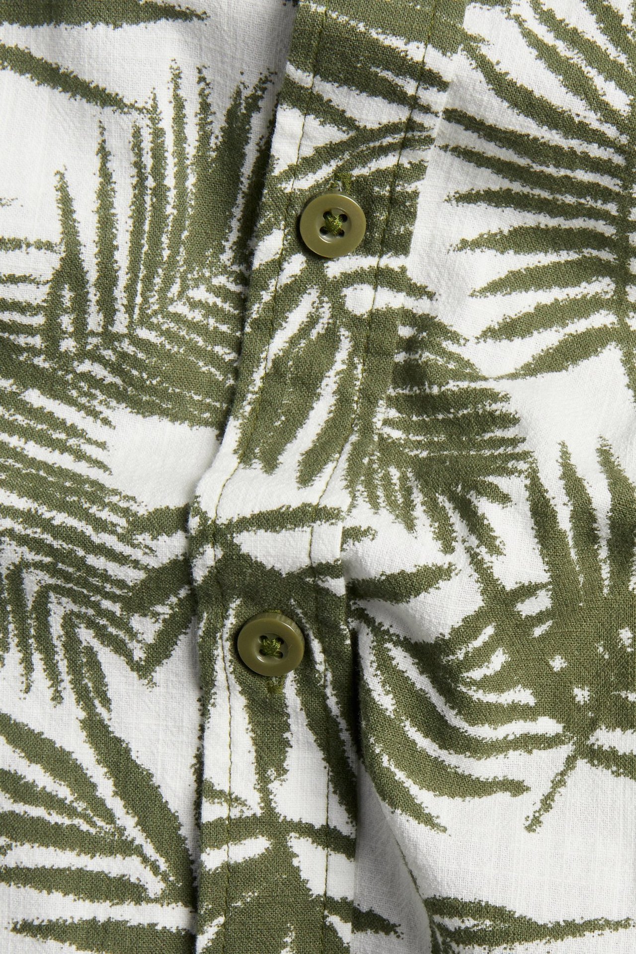 Lähikuva valkoisesta puuvillapaidasta, jossa khakinvihreä palmulehtikuvio ja yhteensopivat vihreät napit.
