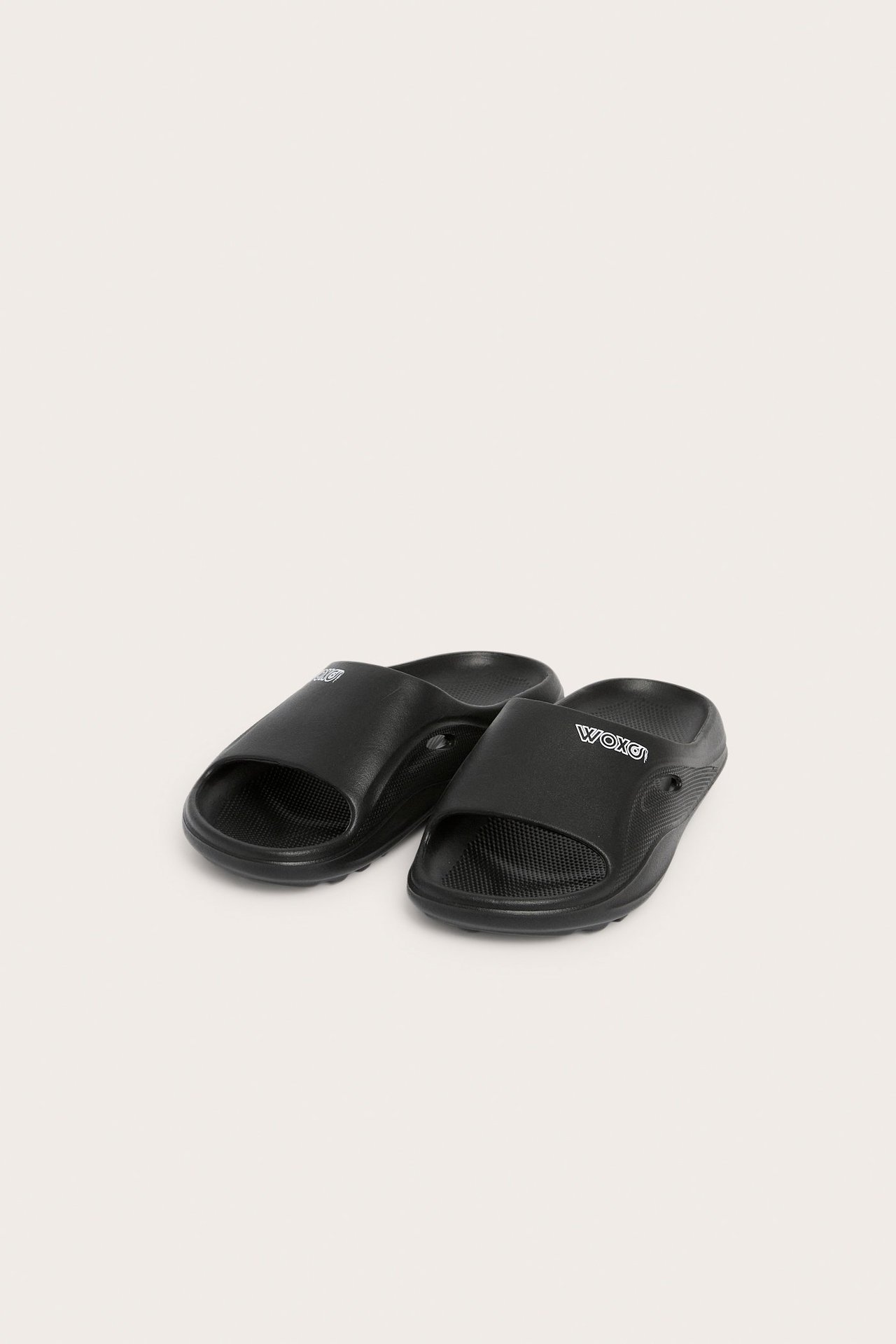 Viisto etukuva kahdesta yksivärisestä mustasta muovisandaalista, joissa valkoiset logot remmeissä.