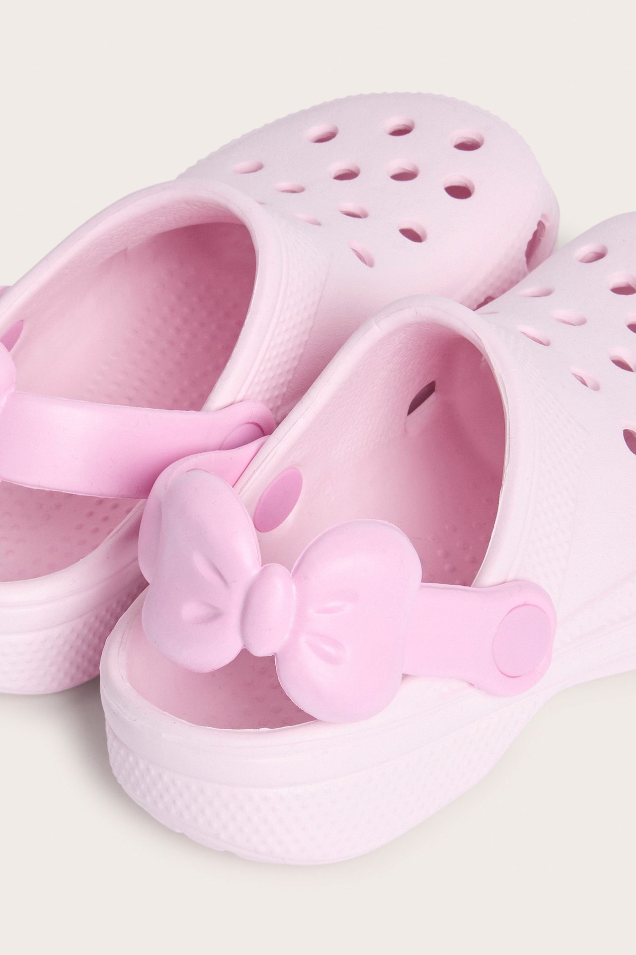 Zbliżenie na jasnoróżowe, plastikowe klapki z ozdobną kokardą na pasku z tyłu.