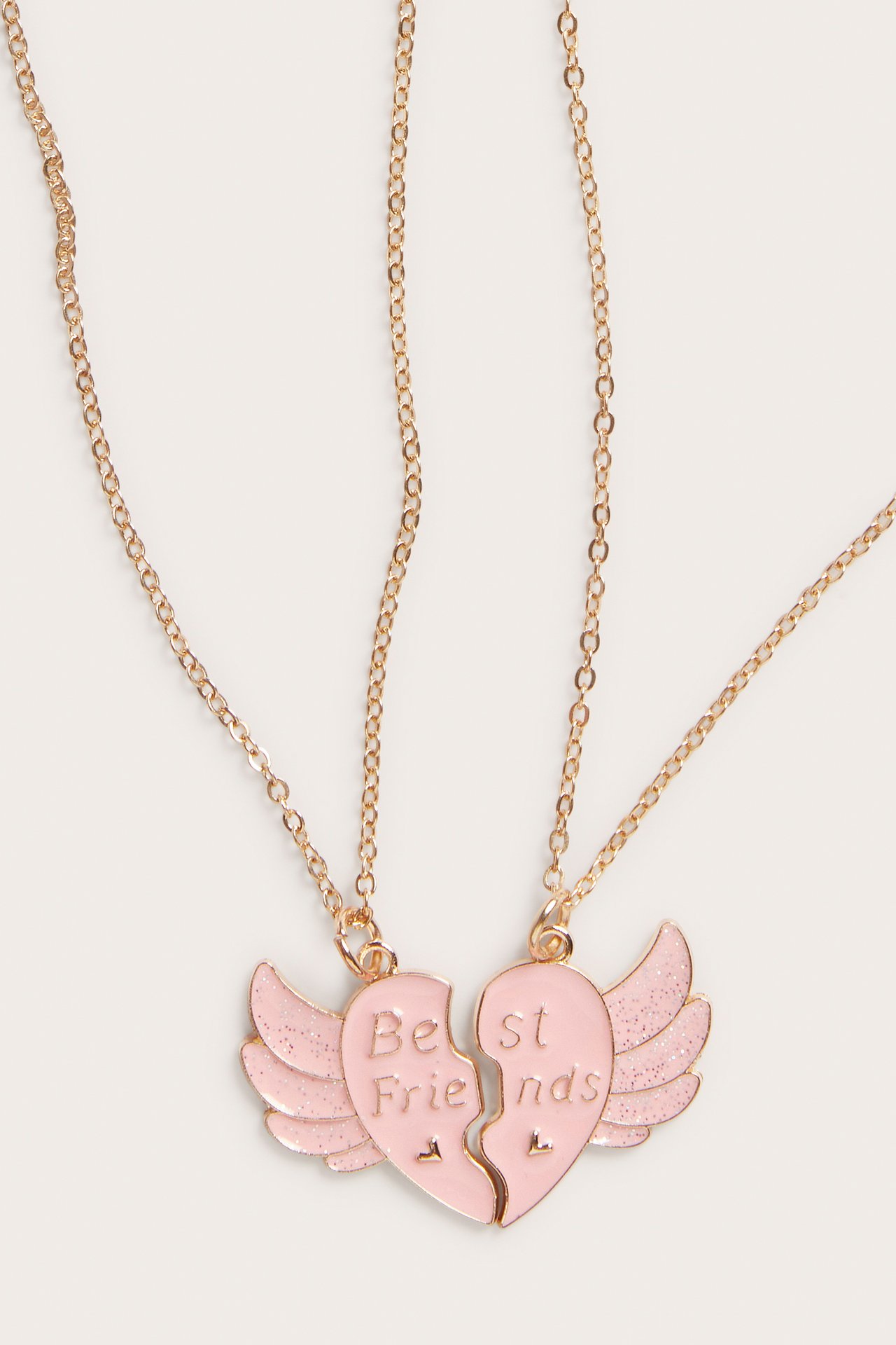 Zbliżenie dwóch metalowych naszyjników przyjaźni z różowymi, brokatowymi zawieszkami w kształcie serc ze skrzydłami.