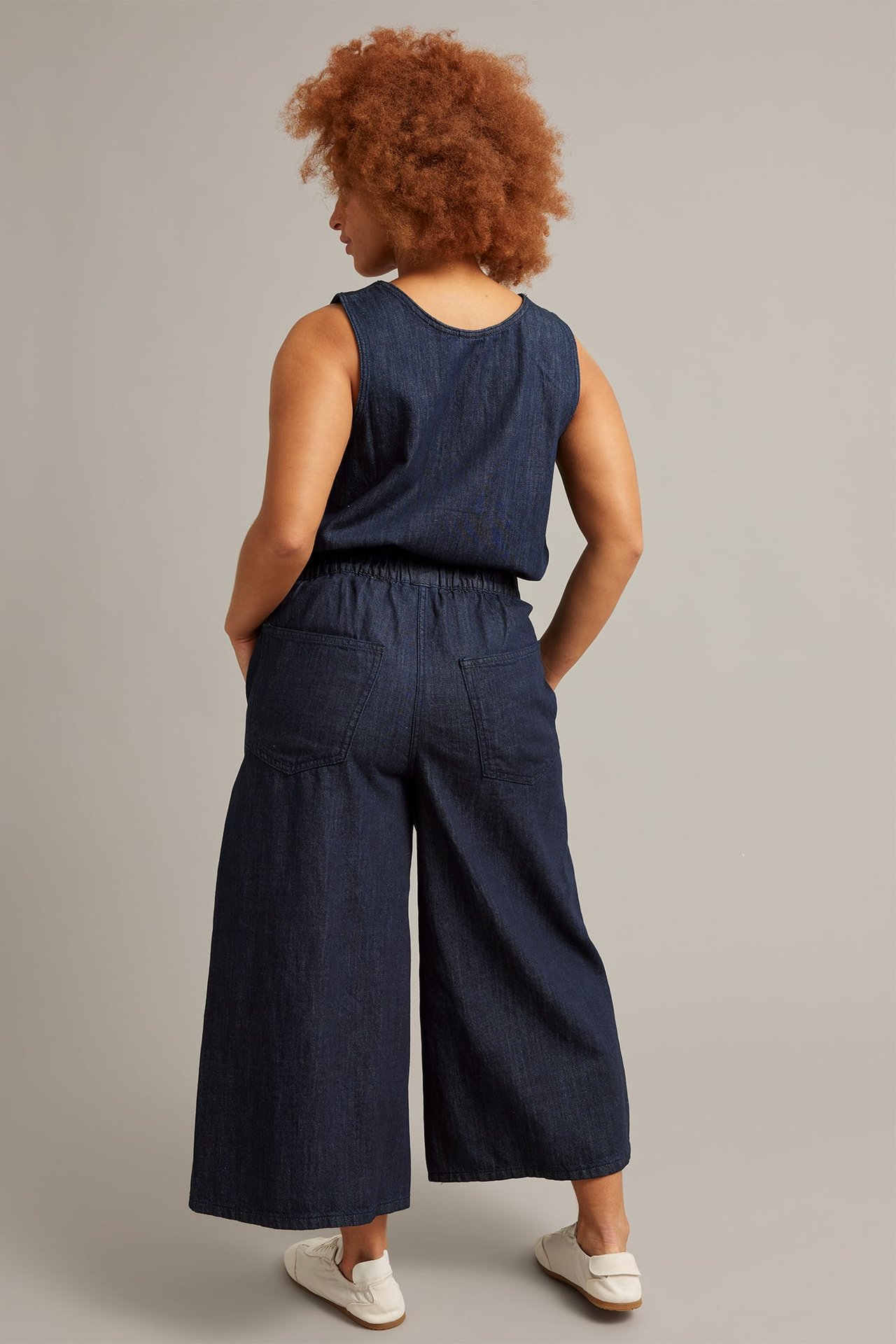 Bakfra: Kvinne i mørke denim pull-on culotte-jeans med ermeløs topp og hvite sko.