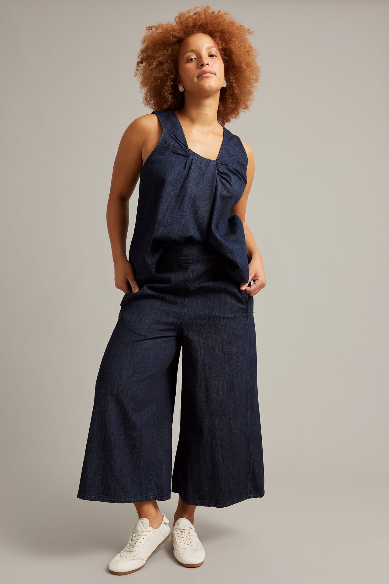 Etukuva: nainen tummissa denim culottes-farkuissa, yhteensopivassa hihattomassa topissa ja valkoisissa lenkkareissa.