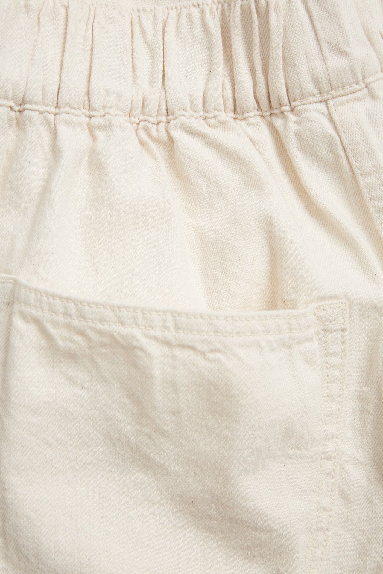 Zbliżenie beżowych jeansów culotte typu pull-on z bawełnianego denimu z elastyczną talią i kieszenią boczną.