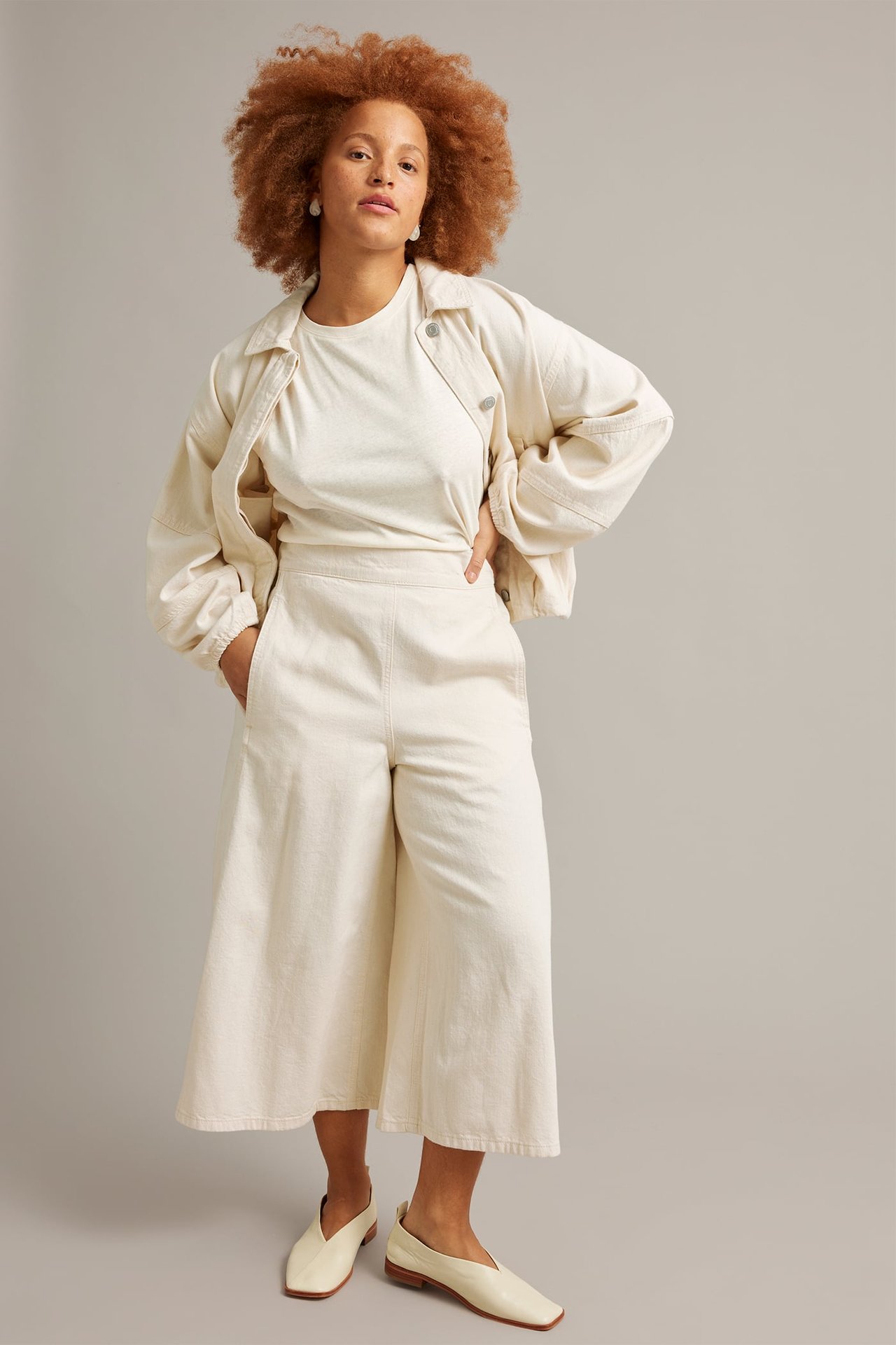 Frontvisning: kvinne i beige bomulls-culottejeans, matchende t-skjorte, jakke og flate sko.