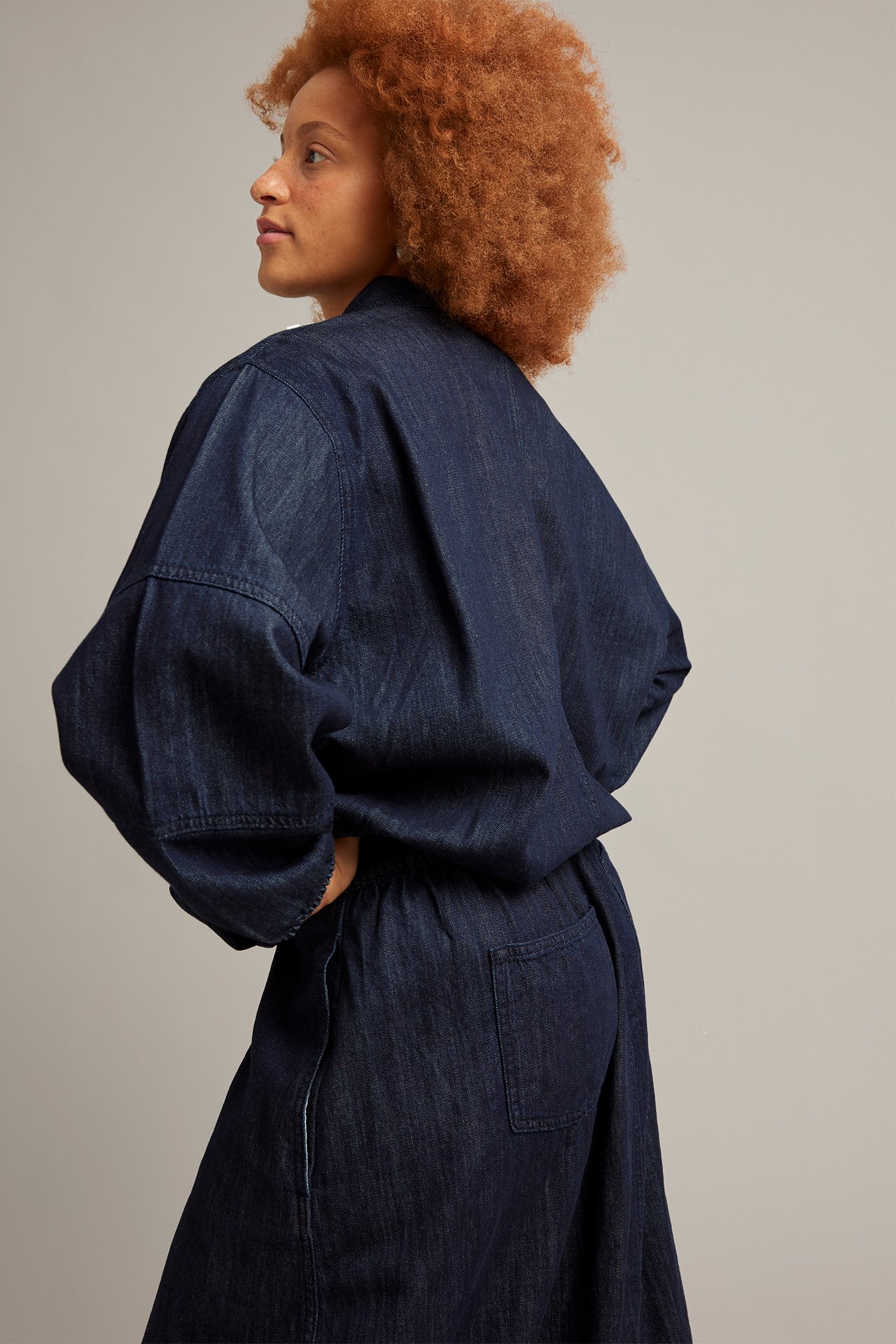 Sivukuva naisesta tummansinisessä denim-blusonitakissa, jossa leveät hihat ja yhteensopivat denimhousut.