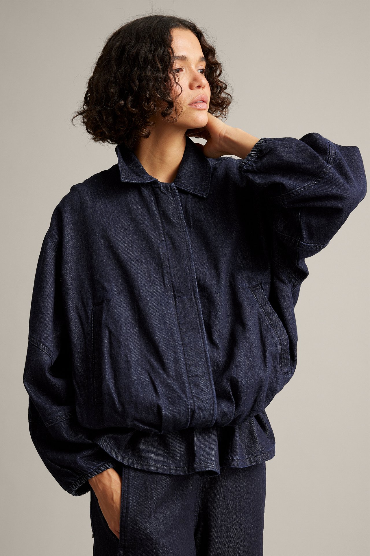 Framifrån, mörkblå oversized jeansbomberjacka med matchande byxor på en kvinna.