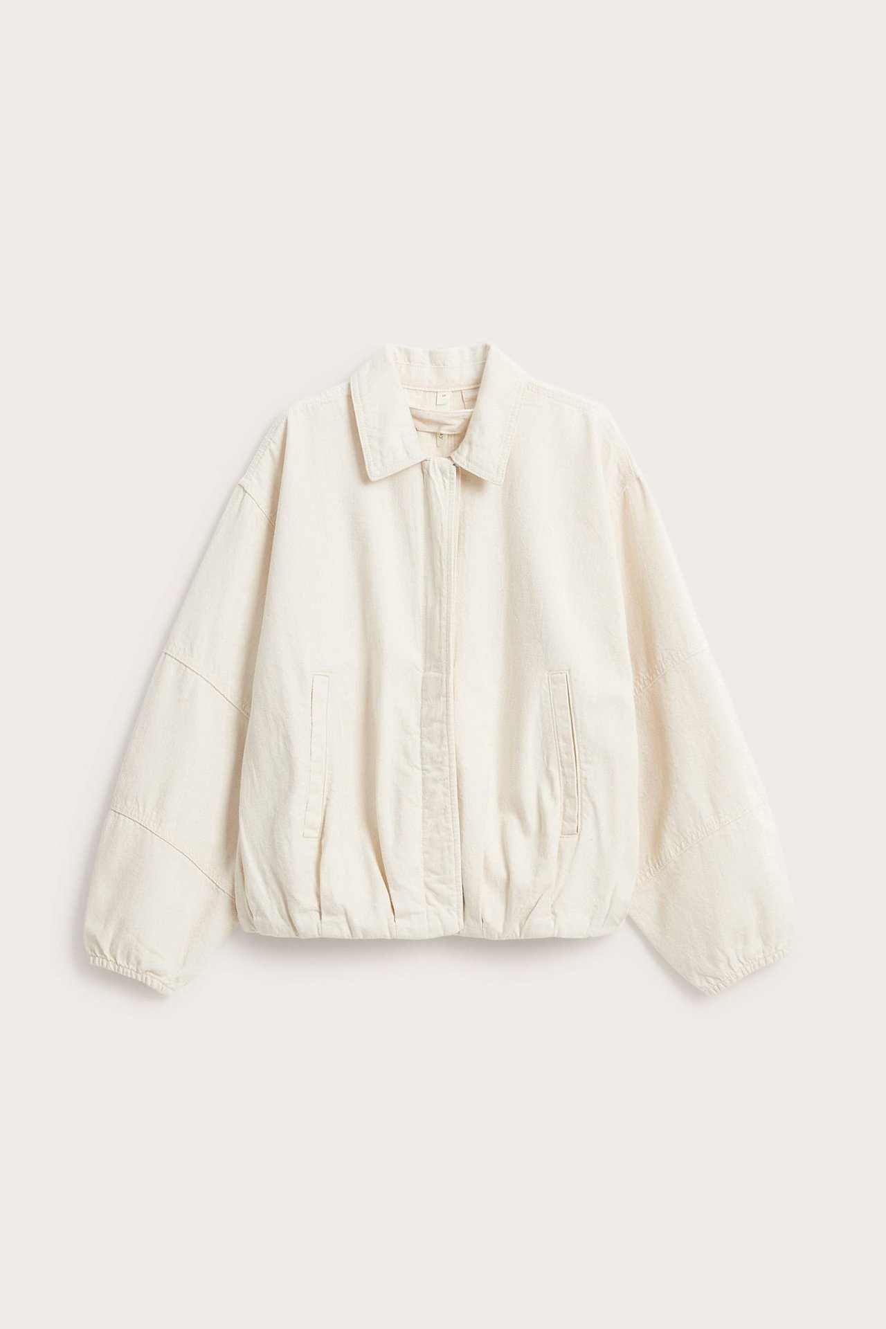 Edestä: Vaalea beige puuvilladenim-bomber-takki, jossa kaulus, piilonapit ja etutaskut.