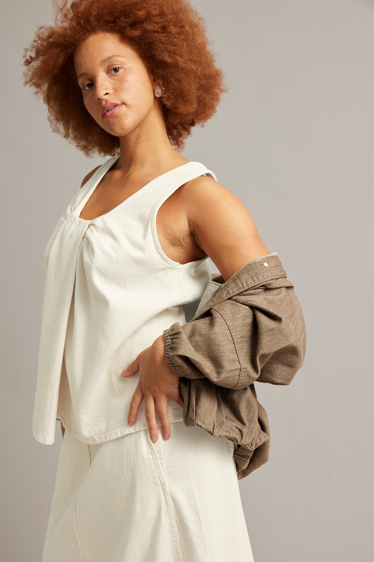 Front view: kvinna bär beige denimlinne med omlottdetalj, matchande kjol och en brun jacka.