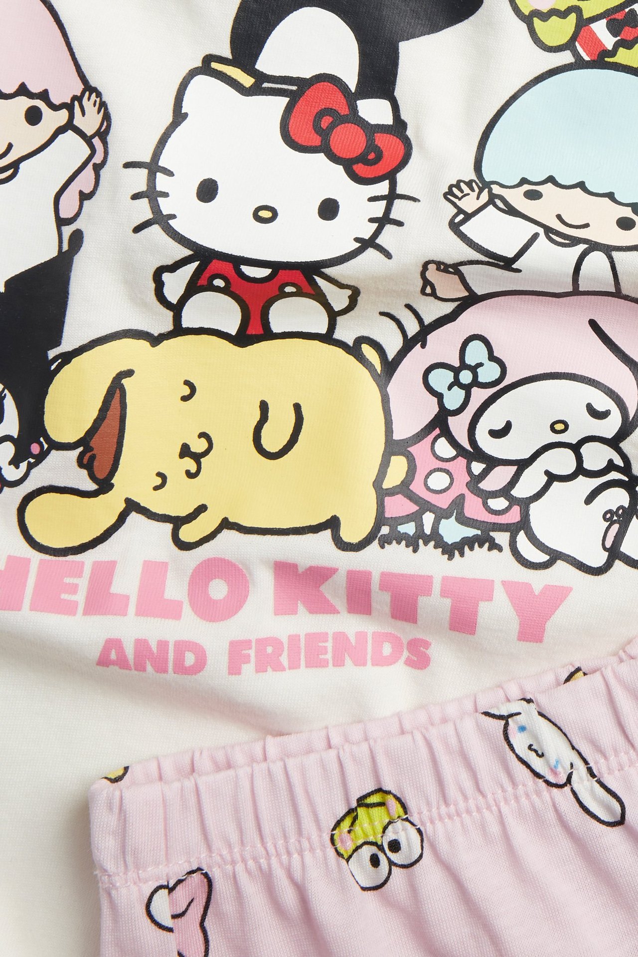 Närbild av ett offwhite kort pyjamas-set i bomull med Hello Kitty-tryck och ljusrosa shorts.