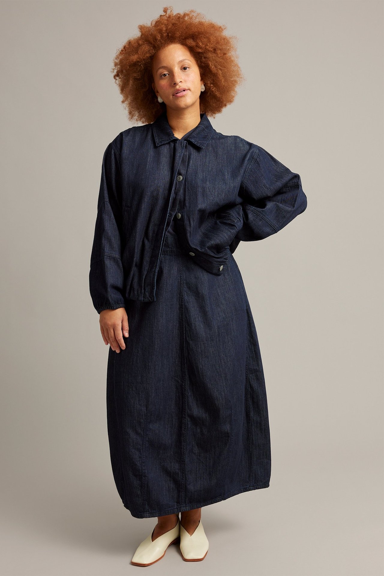 Nainen edestäpäin tummassa denim-barrelhameessa, yhteensopivan farkkutakin ja vaaleiden kenkien kanssa.