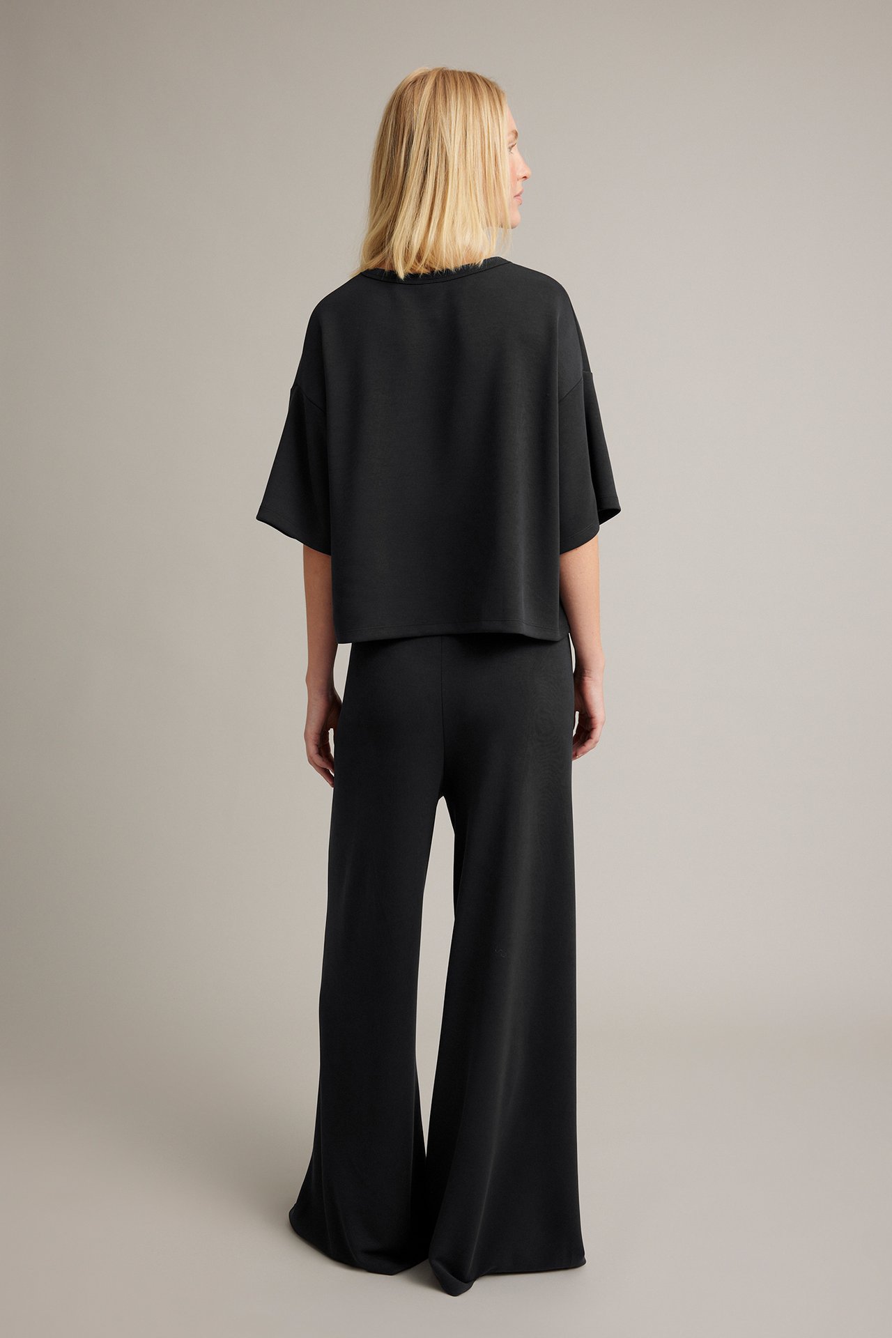 Ryggvy av kvinna i svarta vidbenta byxor och en svart kortärmad croptop.