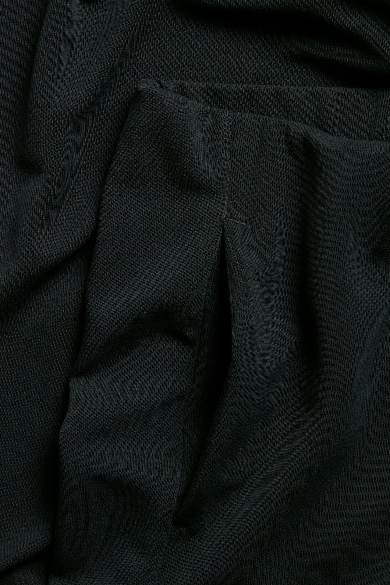 Zbliżenie czarnych dresowych spodni z rozciętą boczną kieszenią i drobnym ściegiem.
