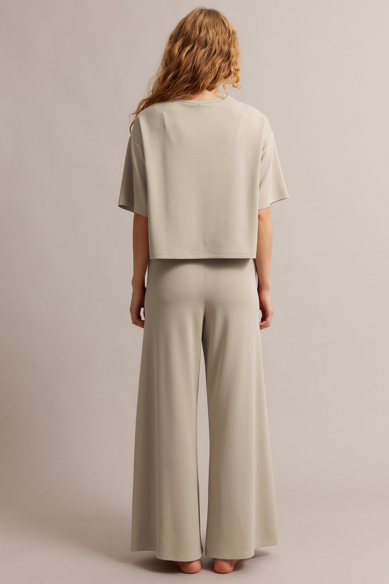 Naisen takakuva: Beiget suoralahkeiset modaalisekoitteiset loungehousut joustovyötäröllä ja yhteensopiva crop-toppi.