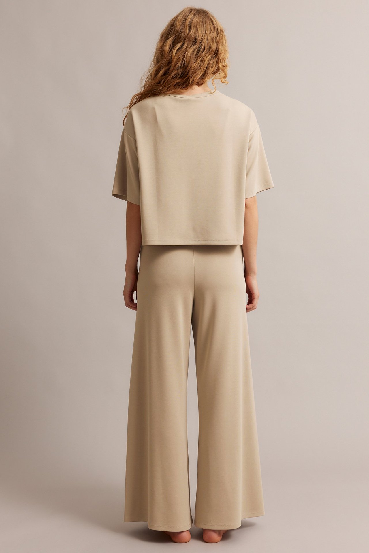 Bakfra, kvinne i beige vide loungebukser og matchende beige kortermet topp.