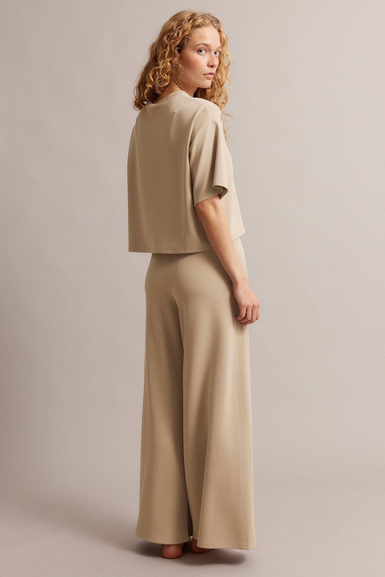 Baksidebilde av en kvinne i beige vide lounge-bukser og en matchende kortermet topp.
