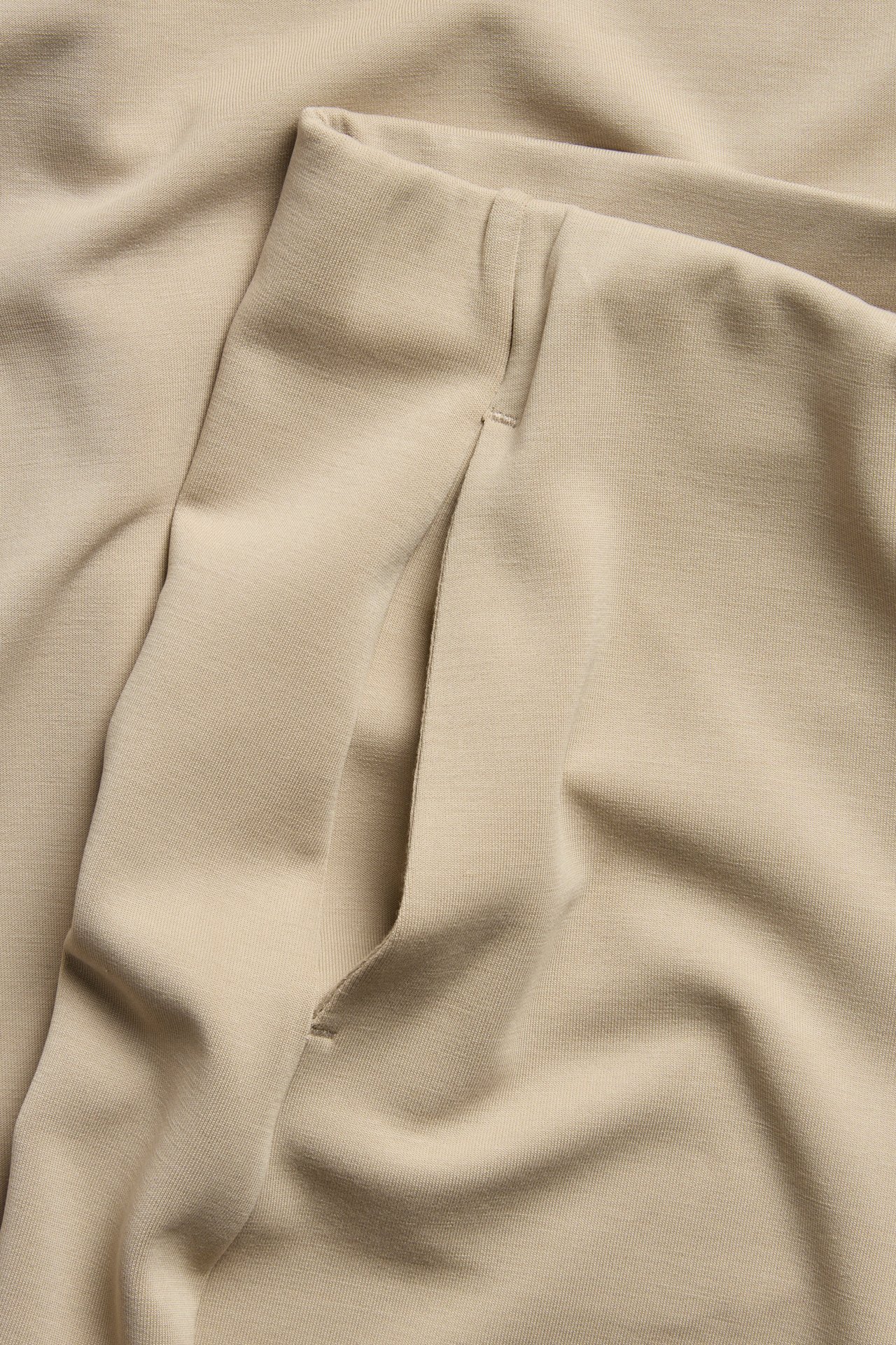 Nærbilde av en beige lounge-bukses sidelomme i mykt modal-blanding stoff.
