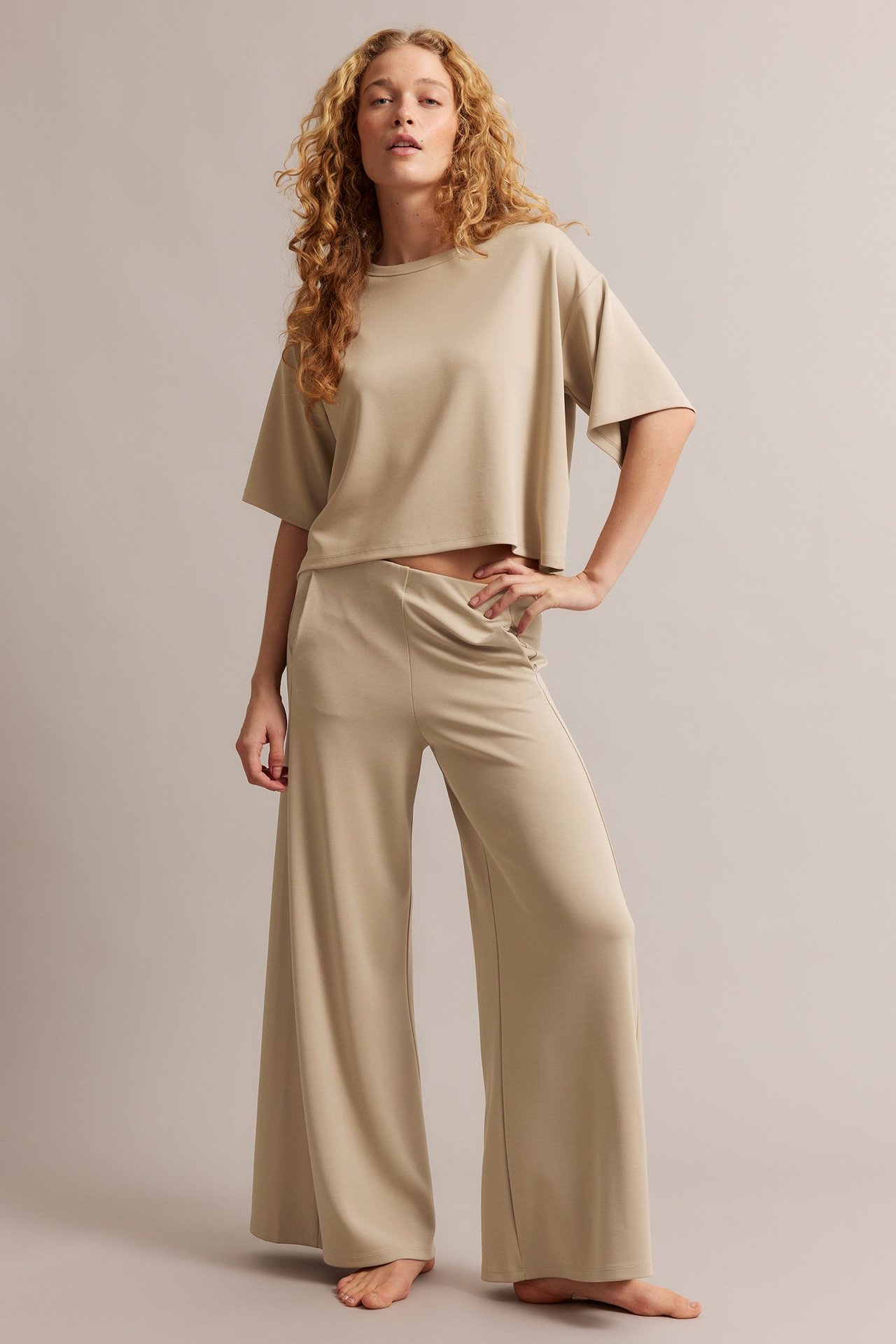 Frontbilde av en kvinne i beige vide loungewear-bukser og en matchende kortermet crop topp.