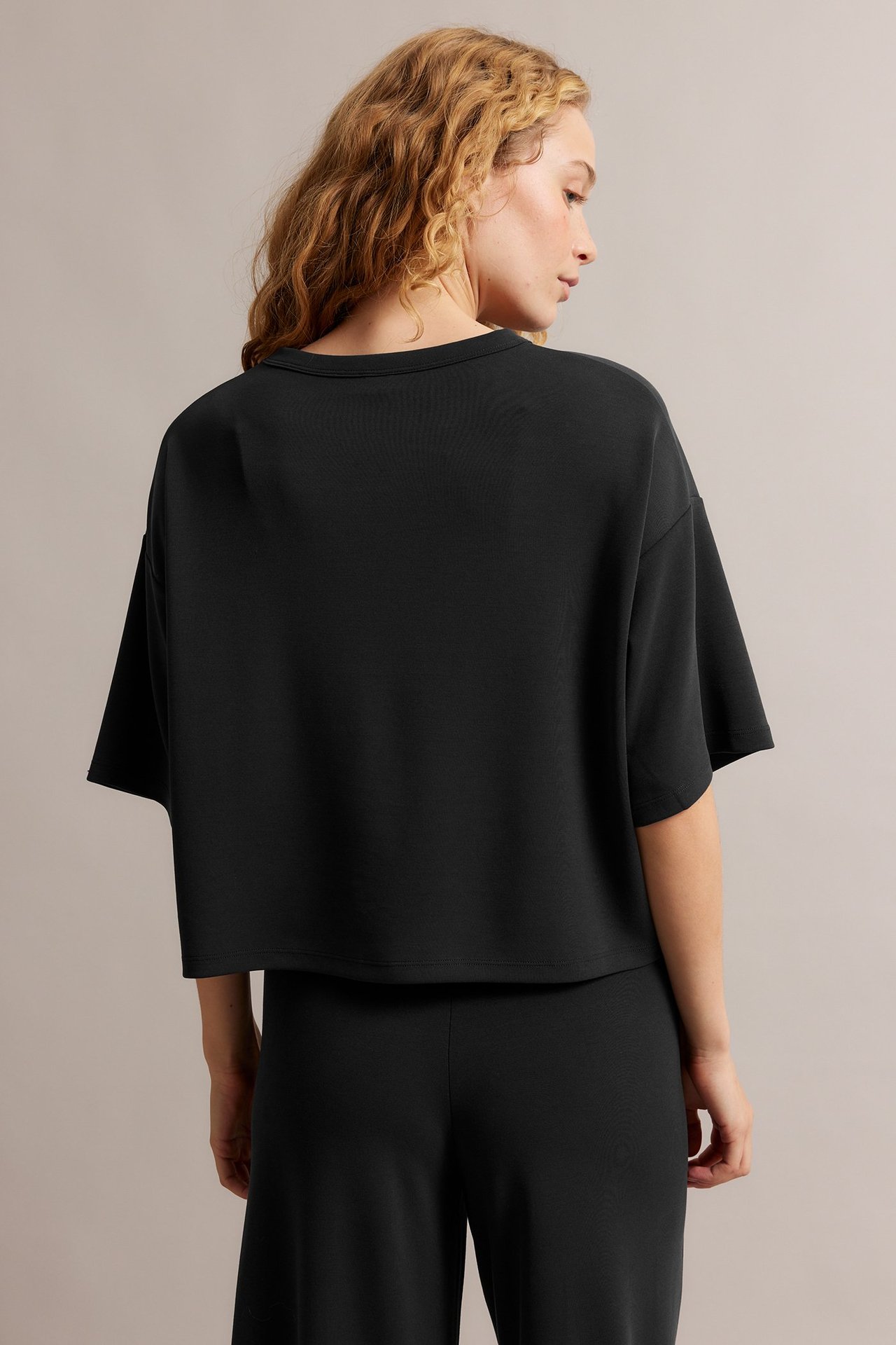Widok z tyłu kobiety w czarnym, pudełkowym T-shircie z krótkimi rękawami i czarnych spodniach.