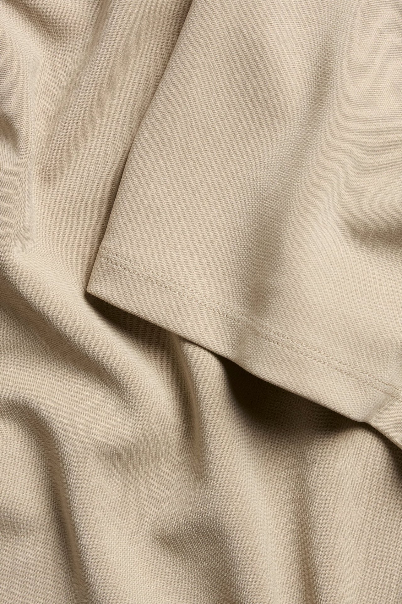 Nærbilde av en beige T-skjorte, som viser dens myke modalblandingsstoff med subtile folder og sømmer.