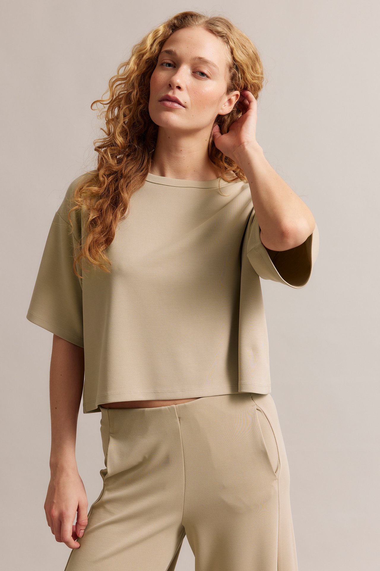 Framifrån: en kvinna bär en beige boxig, kort T-shirt med vida ärmar och matchande beiga byxor.