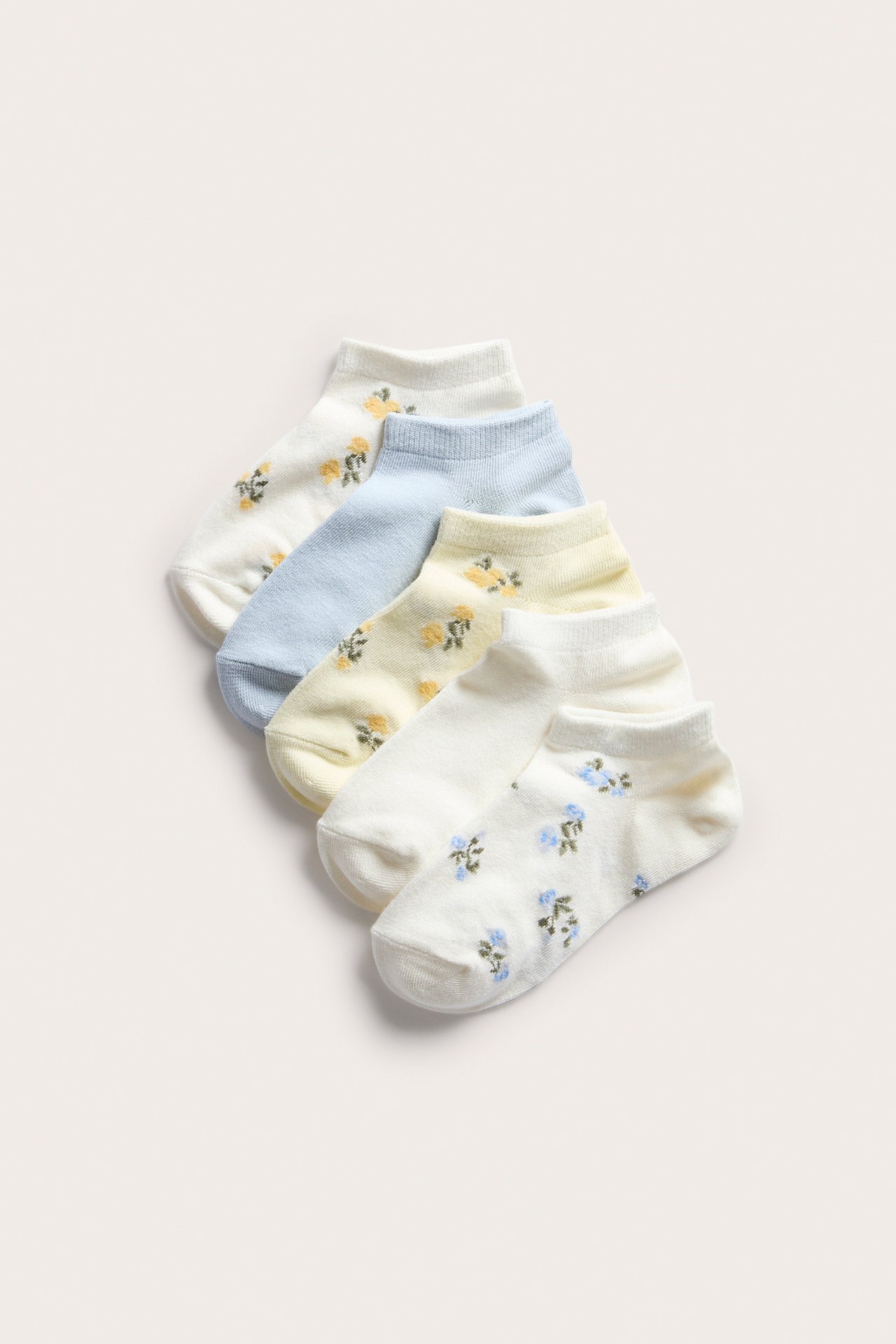 Ovanifrån: 5-pack ankelstrumpor; tre blommiga (offwhite, ljusgul) och två enfärgade (ljusblå, offwhite).