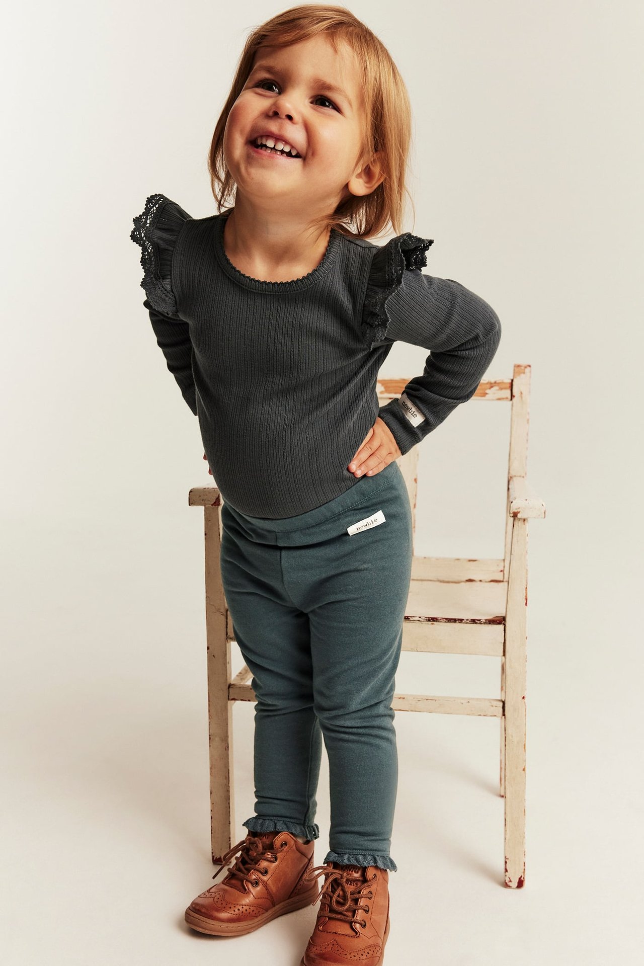 Framsida: flickbarn i mörkgrå ribbad långärmad body, petroleumblå leggings och bruna snörstövlar.