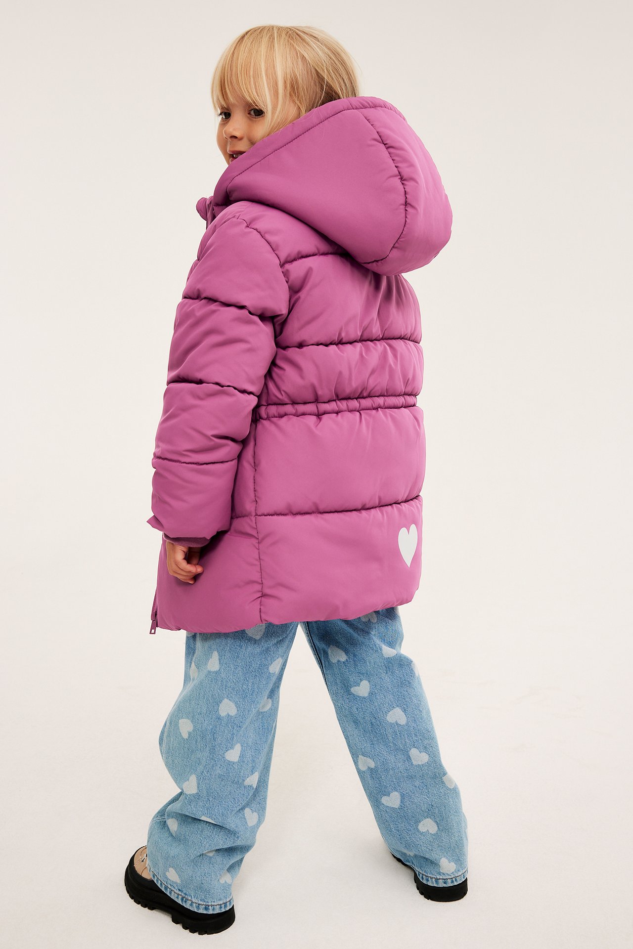 Sidebilde: barn i lilla hettejakke med hvitt hjerte, jeans med hjertemønster og tykke sko.