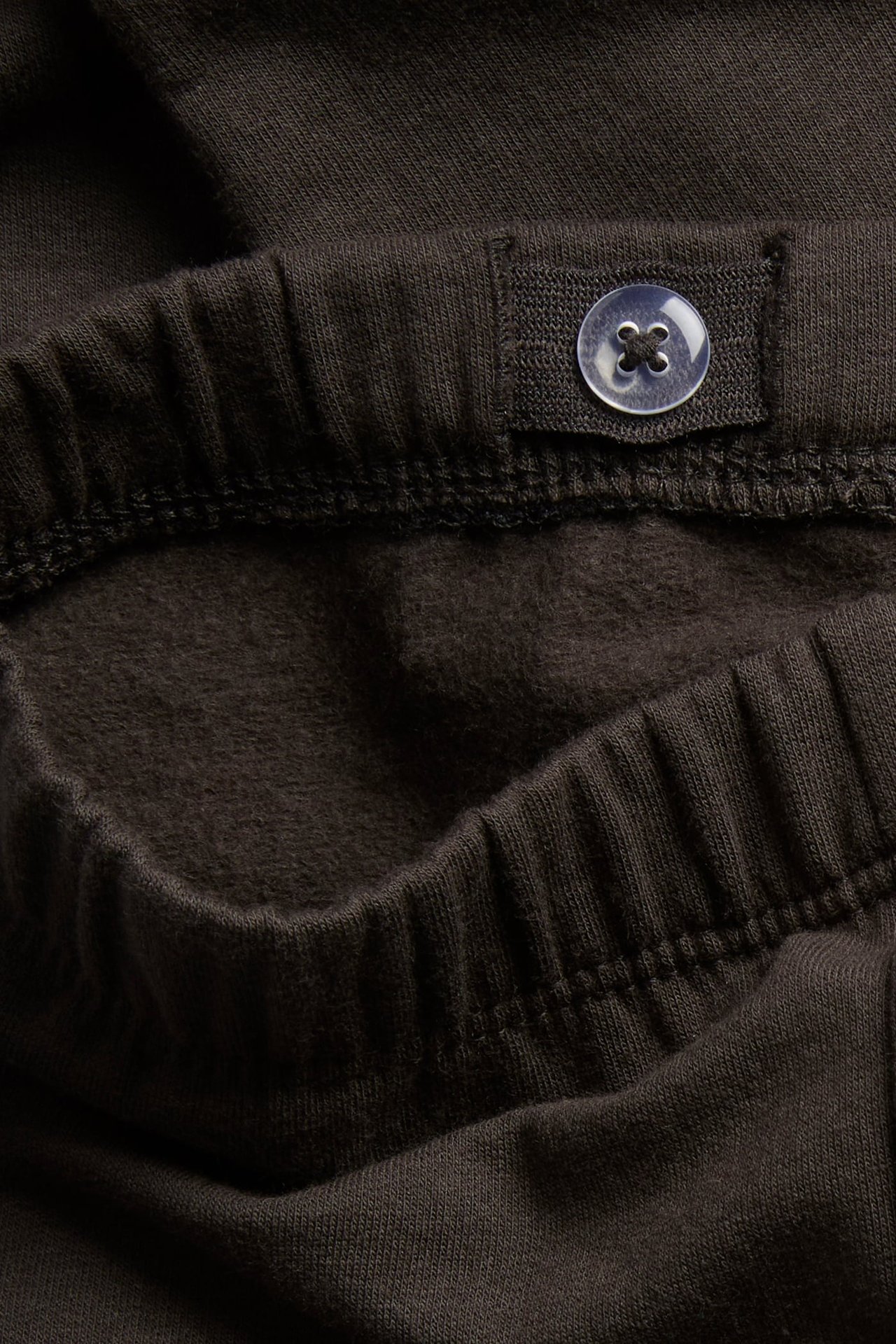 Zbliżenie ciemnobrązowego ubrania z podszewką polarową, elastycznym pasem i przezroczystym guzikiem.