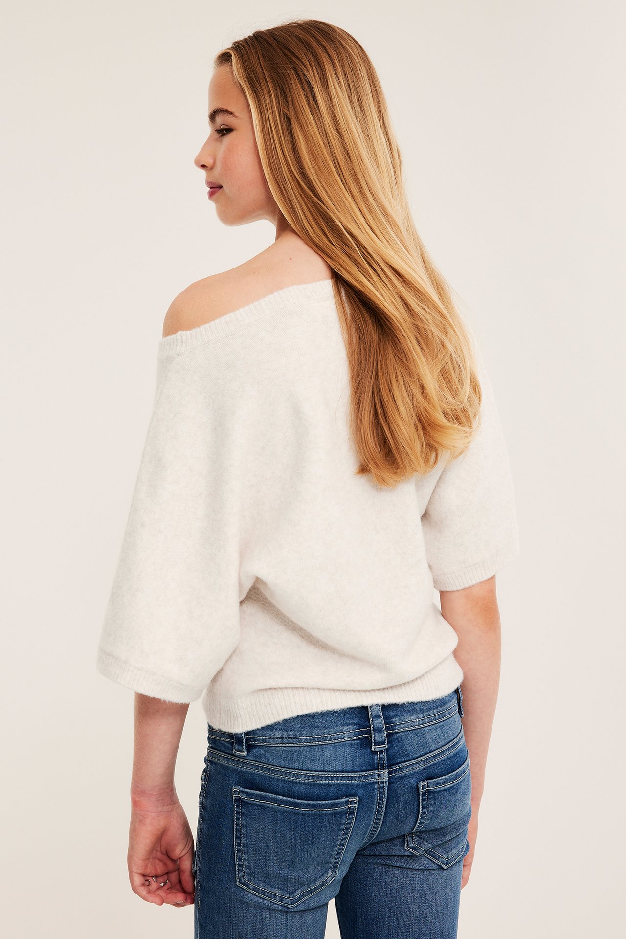 Ryggvy av ett barn i en benvit off-shoulder tröja och blå jeans.