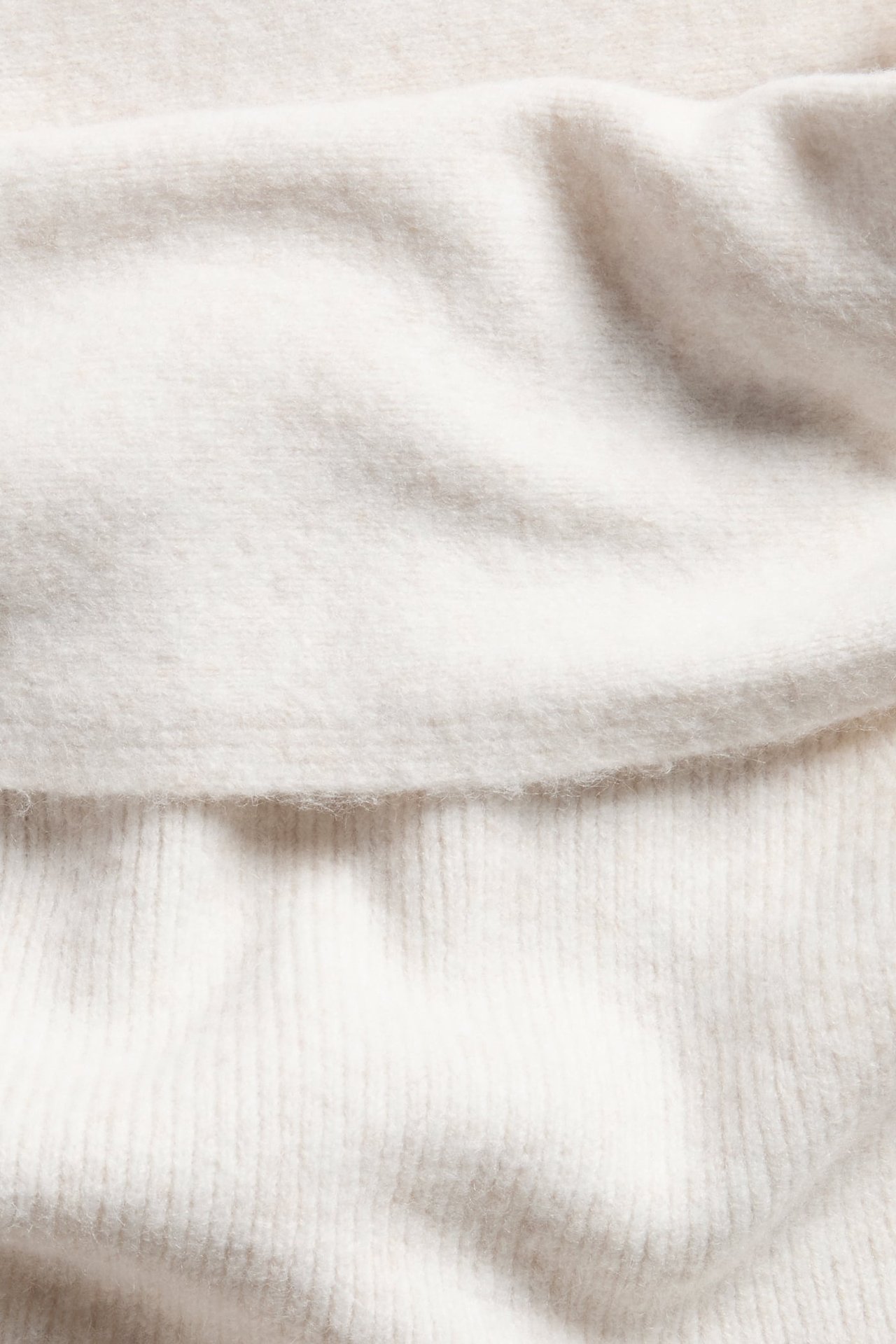 Zbliżenie na biały melanżowy, dzianinowy top off-shoulder z miękką prążkowaną fakturą.