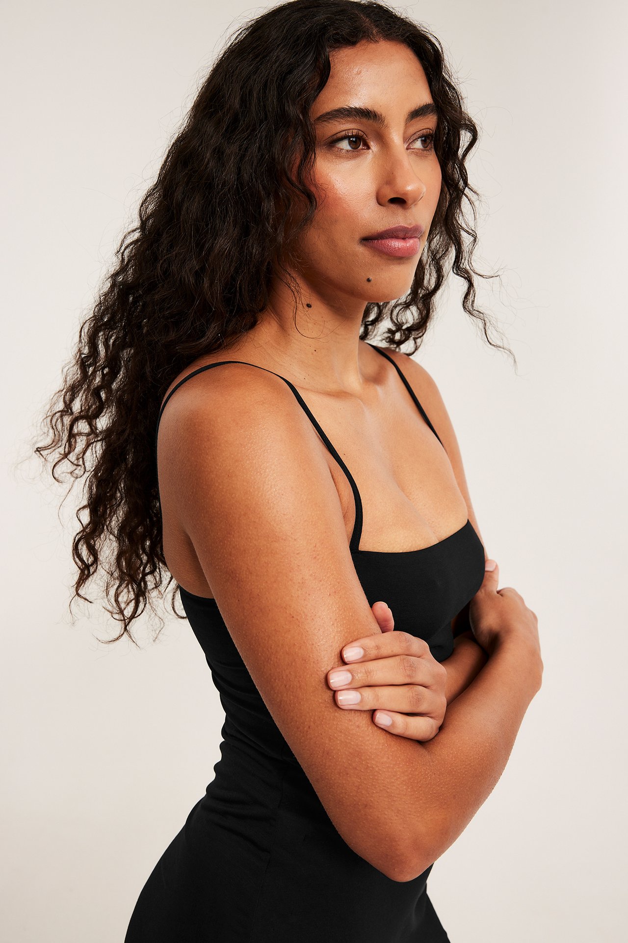 Närbild, sidovy av kvinna i svart underklänning i modalmix med tunna justerbara axelband.