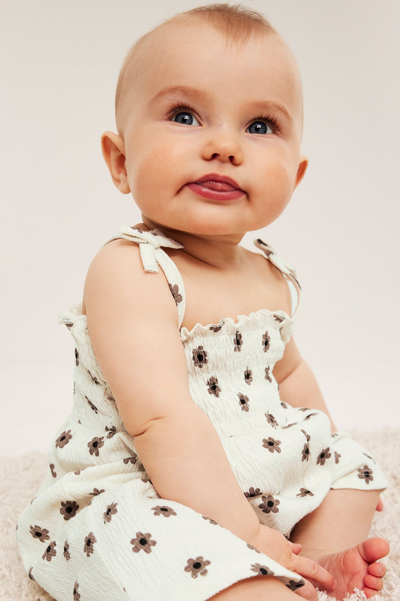 Framifrån: Baby i offwhite smockad blommig krinklad jersey jumpsuit med rosettband.