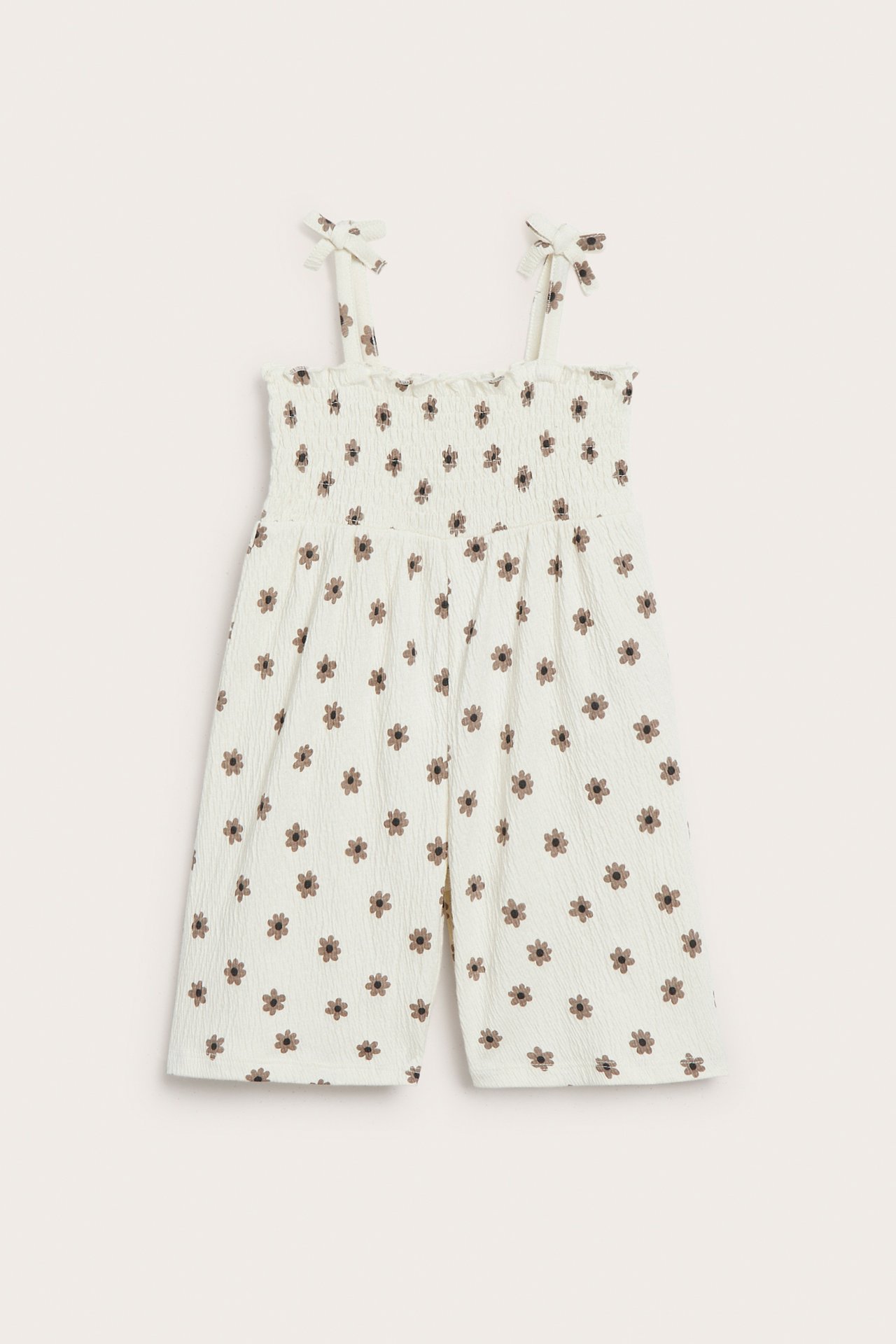 Edestä: luonnonvalkoinen vauvan haalari, ruskea kukkakuvio, smokkirypytetty yläosa, rusettiolkaimet.