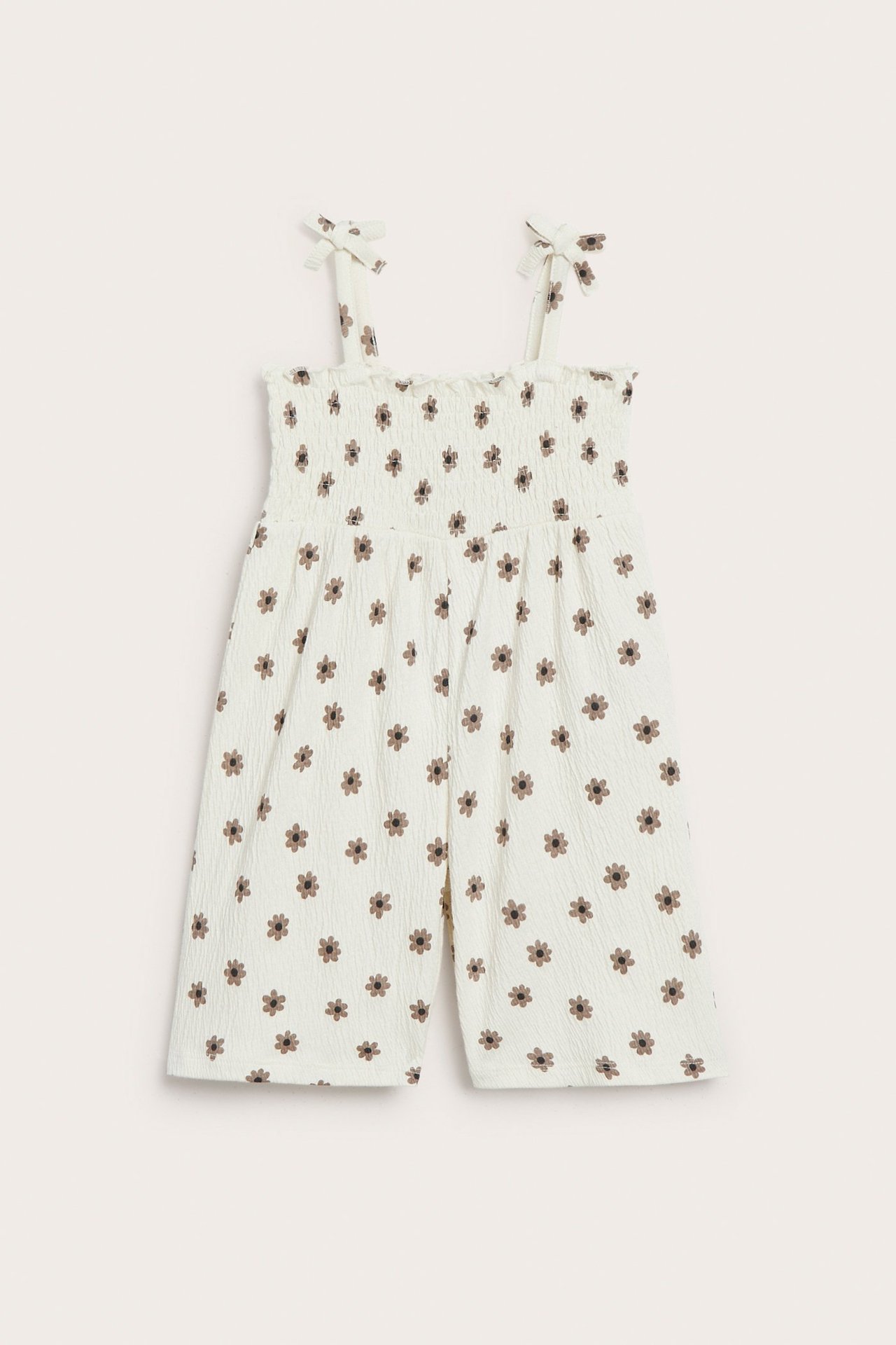 Edestä: luonnonvalkoinen vauvan haalari, ruskea kukkakuvio, smokkirypytetty yläosa, rusettiolkaimet.