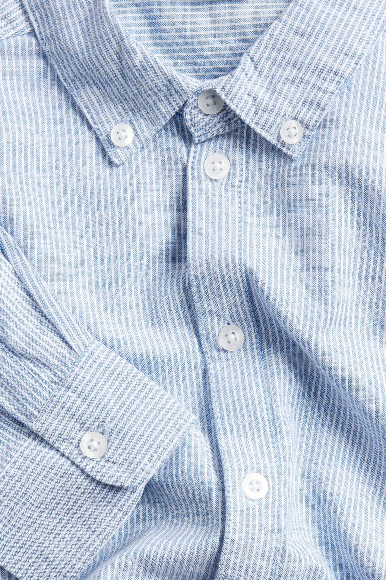 Zbliżenie na paski jasnoniebieskiej koszuli bawełnianej z kołnierzykiem button-down i białymi guzikami.