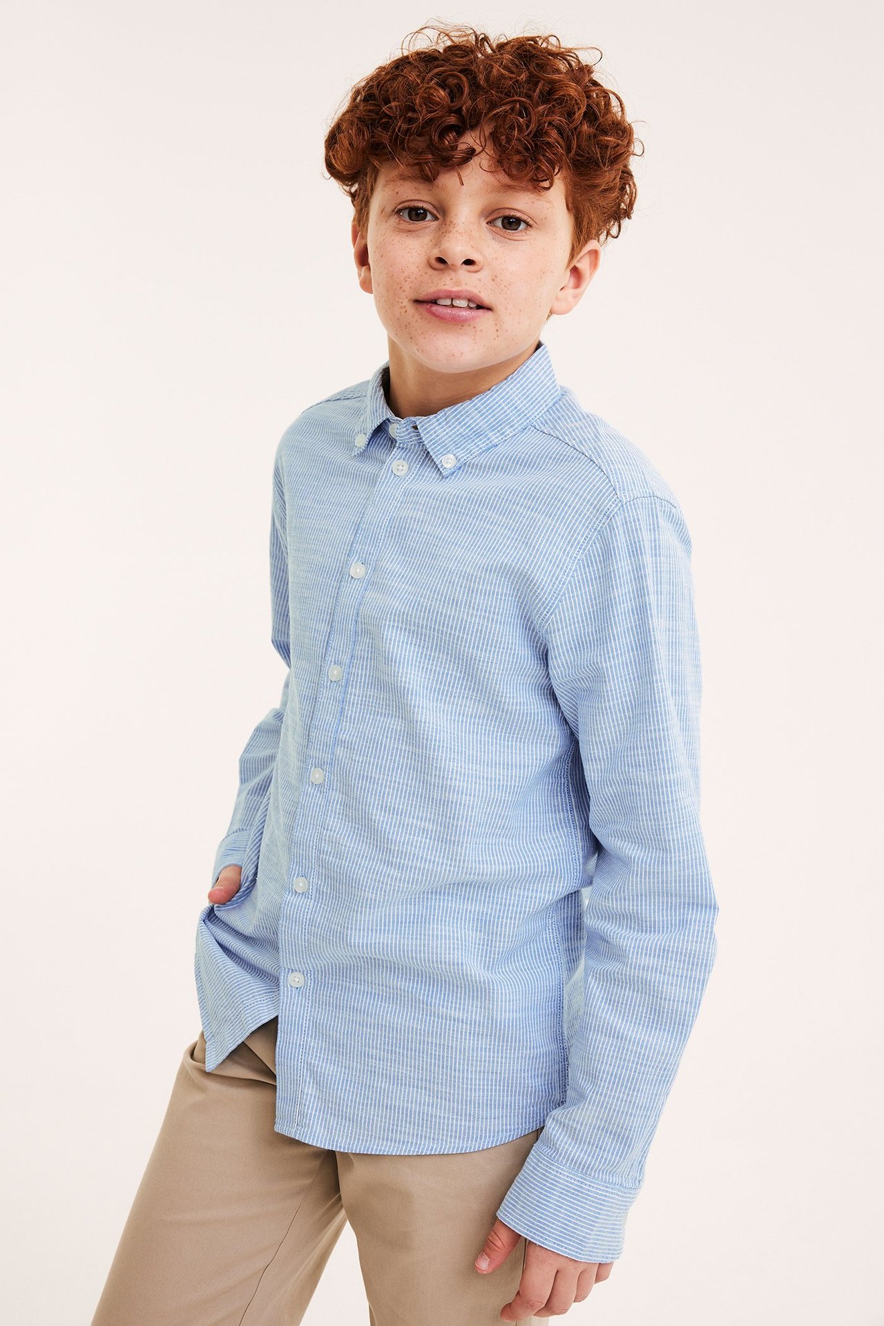 Framifrån: Kid i ljusblå randig bomulls-oxfordskjorta med button-down-krage och beiga byxor.