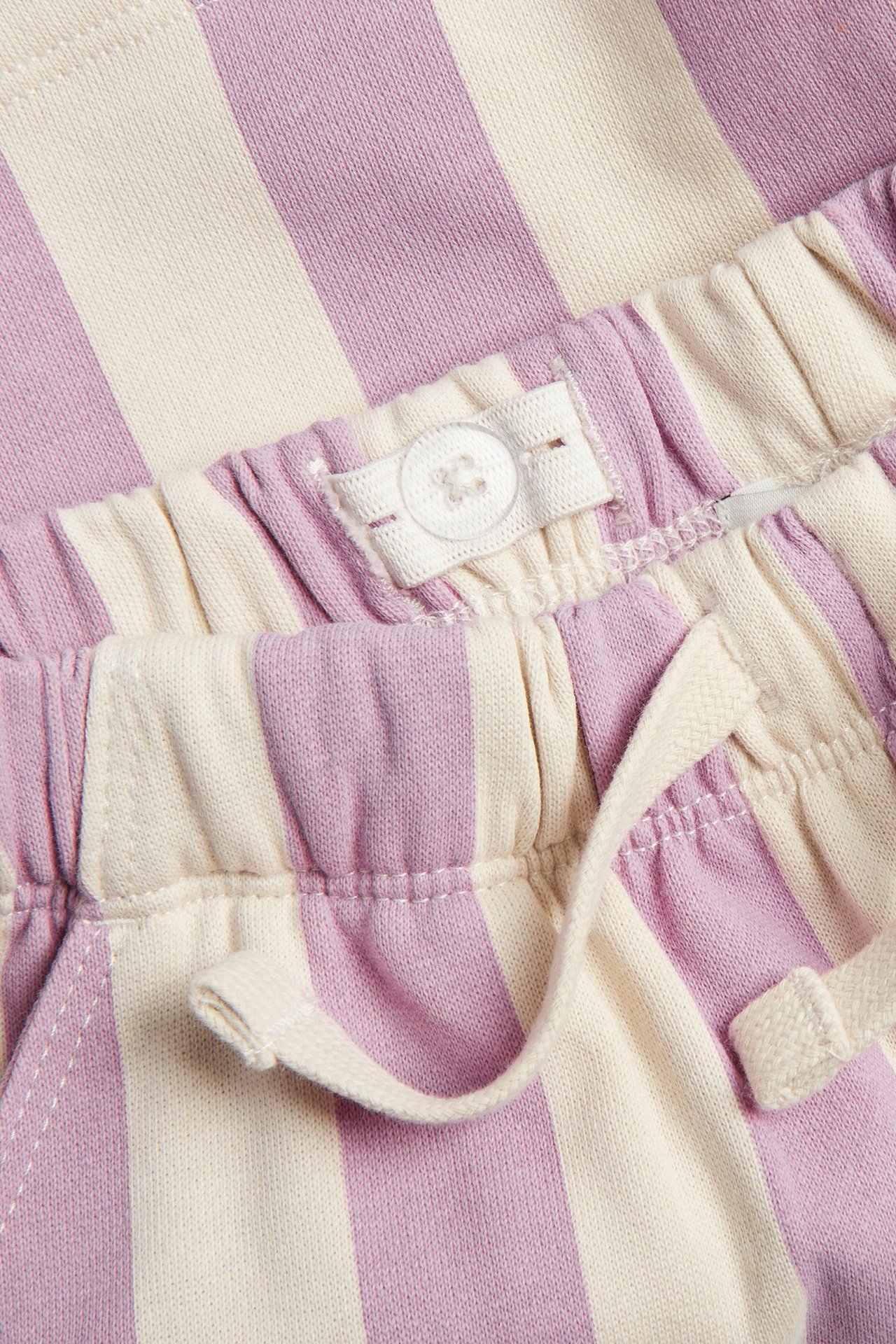 Lähikuva vaaleanpunaisista ja luonnonvalkoisista raidallisista trikooshortseista, säädettävällä joustovyötäröllä ja valenauhalla.