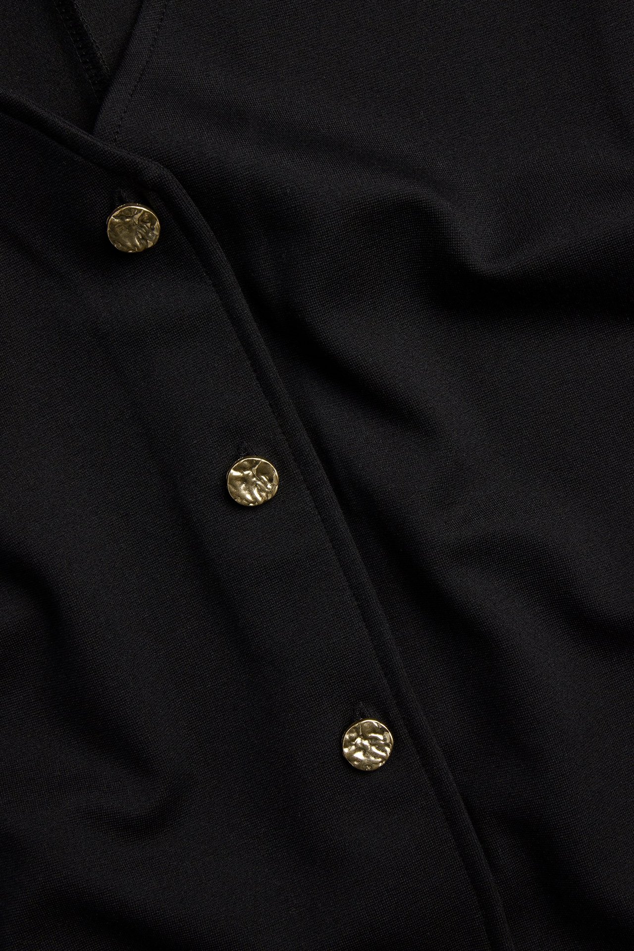 Zbliżenie czarnej kamizelki z dzianiny z trzema młotkowanymi, złotymi guzikami z przodu.