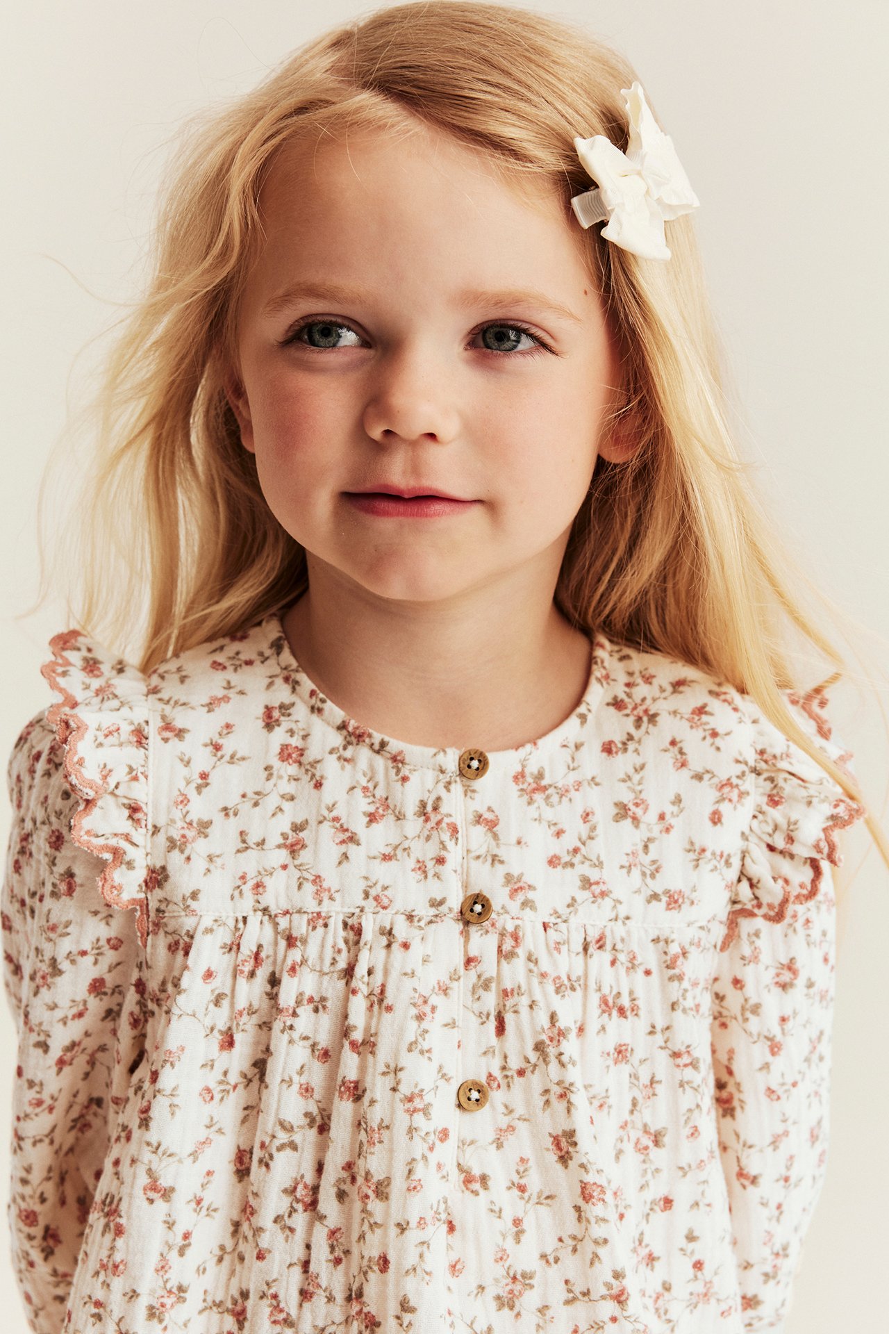 Frontbilde av barn i offwhite småblomstret muslinbluse med skulderkanter og knapper foran.