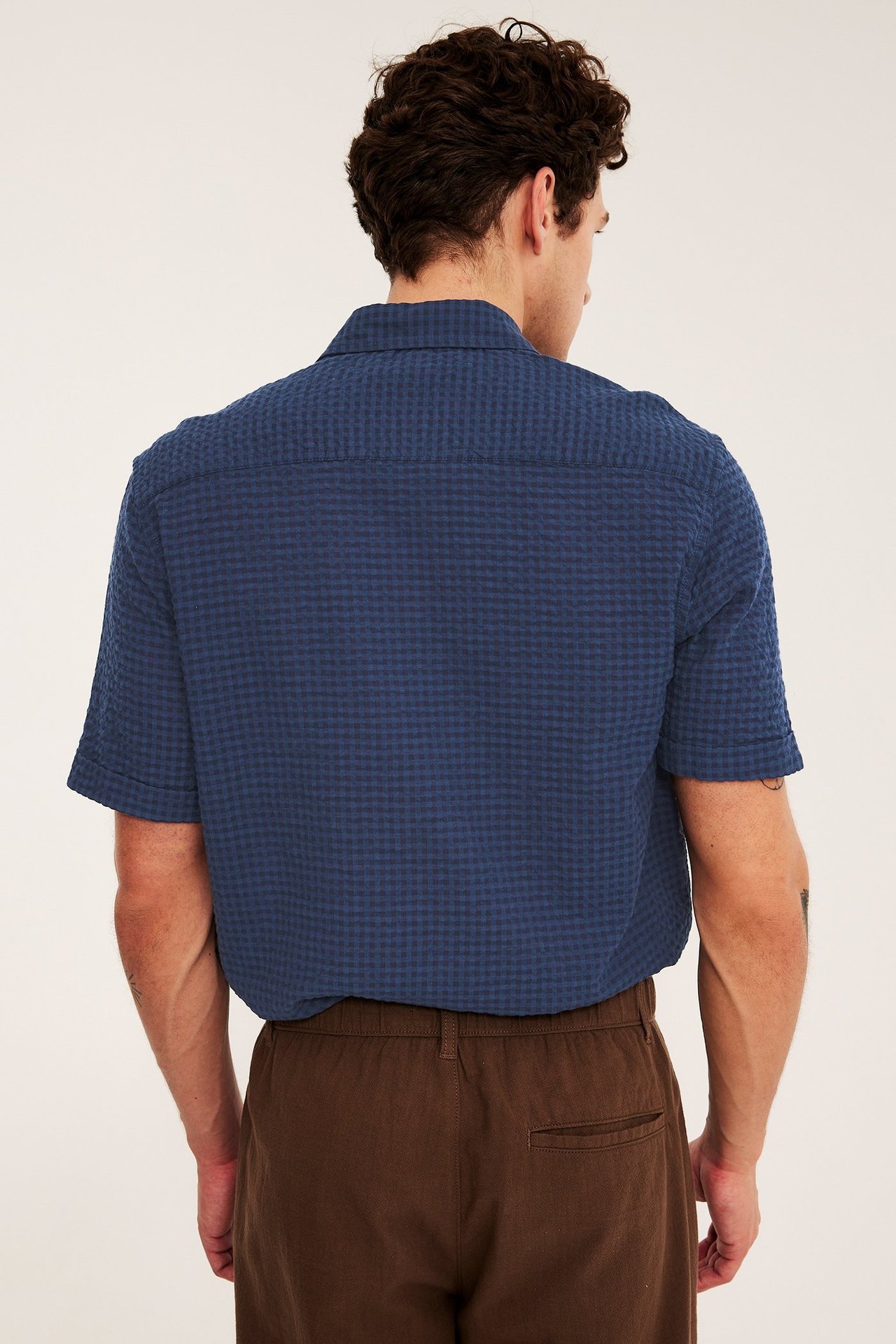 Man, bakifrån, i blårutig kortärmad bäckeböljeskjorta och bruna byxor.
