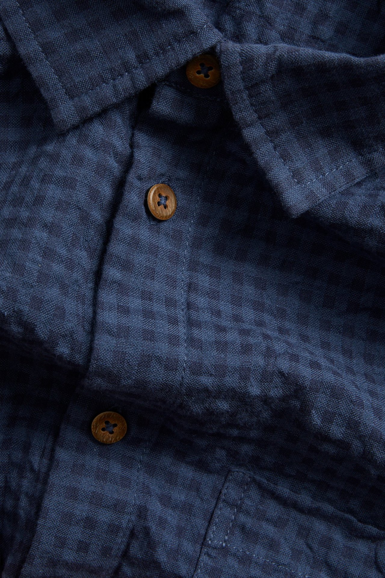 Zbliżenie niebieskiej, krótko rękawowej koszuli w kratę, z kieszenią i drewnianymi guzikami.