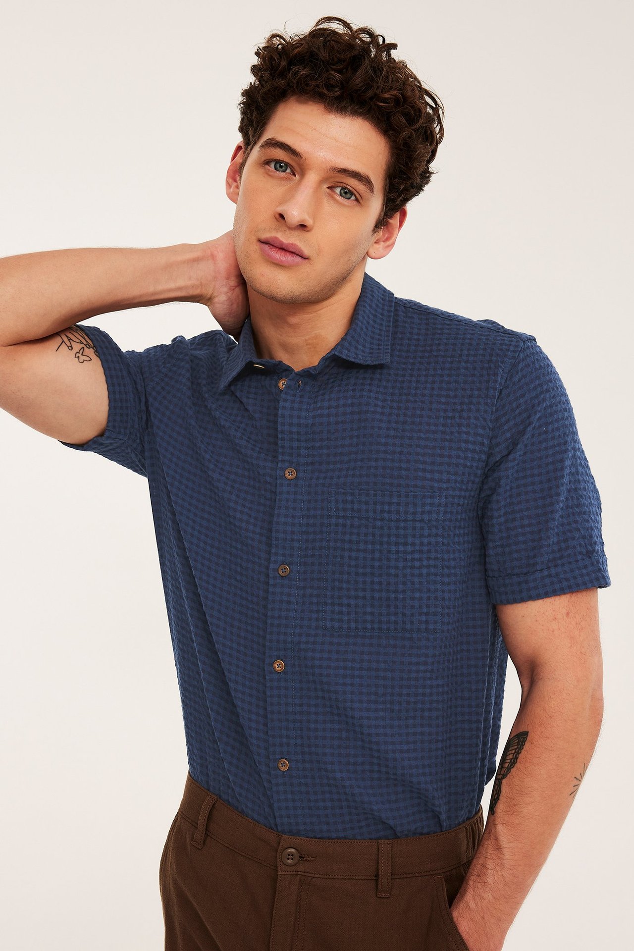Framsida av en man som bär en blårutig kortärmad skjorta med ficka och bruna byxor.