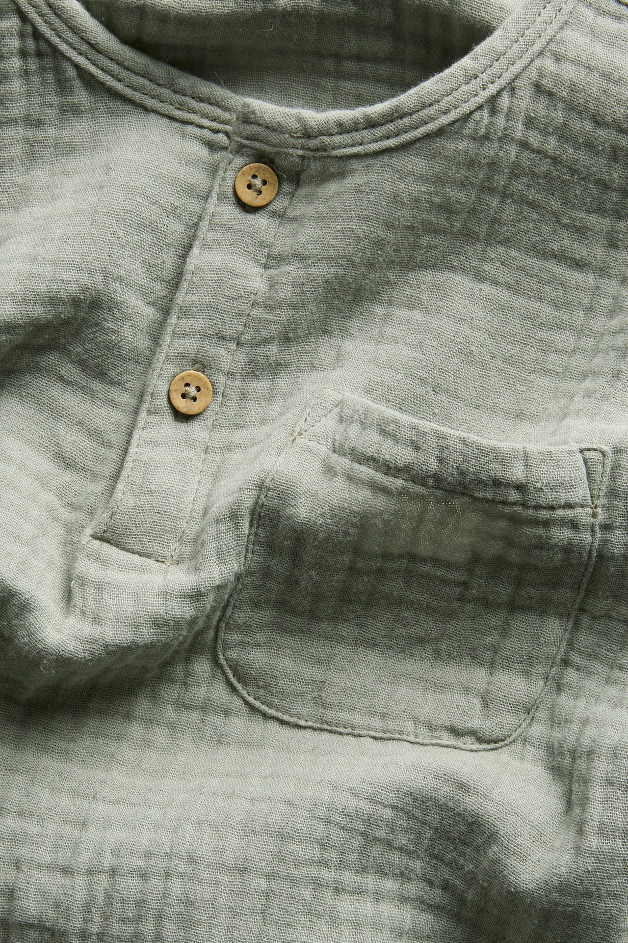 Zbliżenie z przodu jasnozielonej bluzki z długim rękawem z muślinu bawełnianego z listwą guzikową i kieszenią.