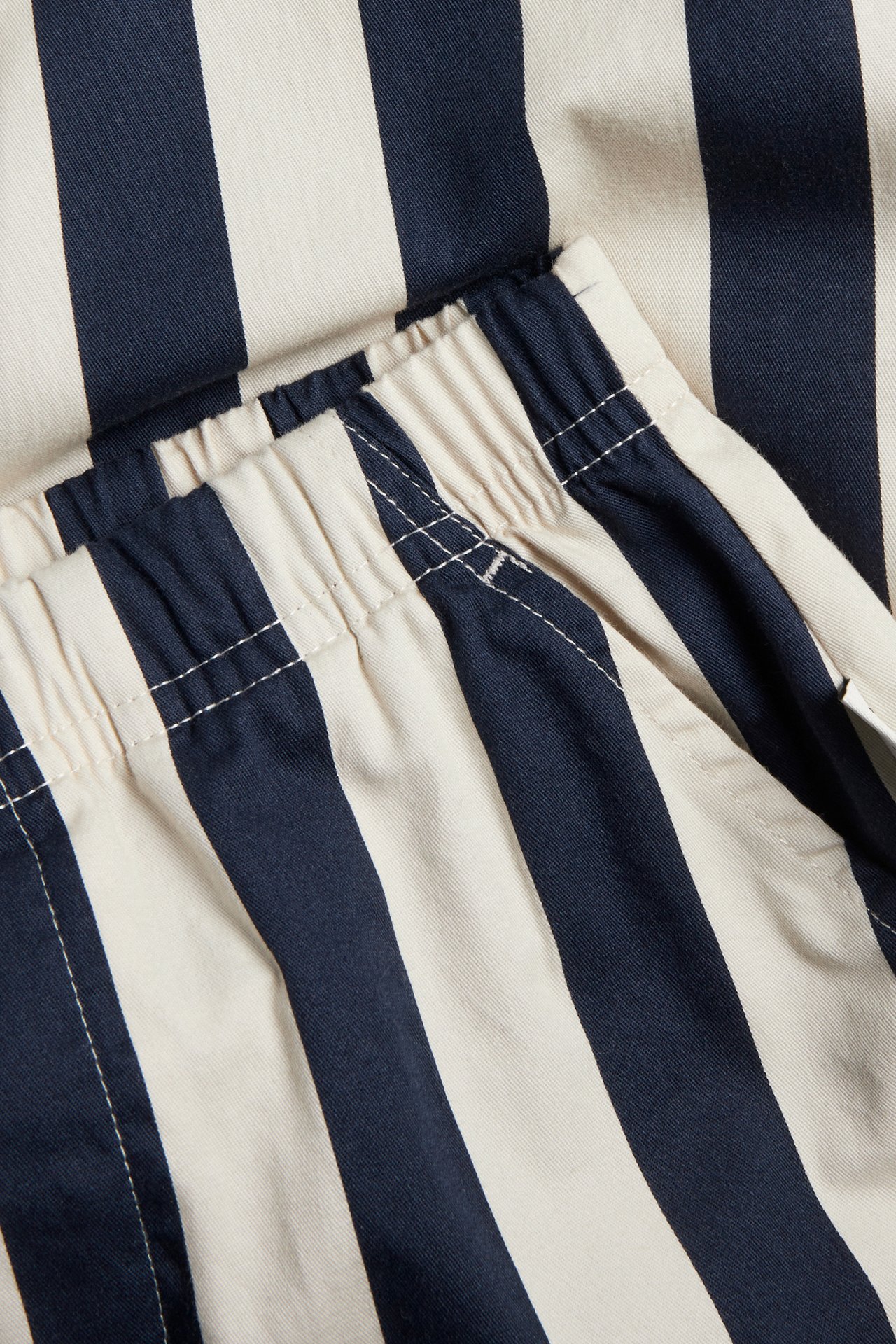 Närbild på vävda mörkblå och off-white randiga bomullsbyxor för barn med resårmidja och sidficka.