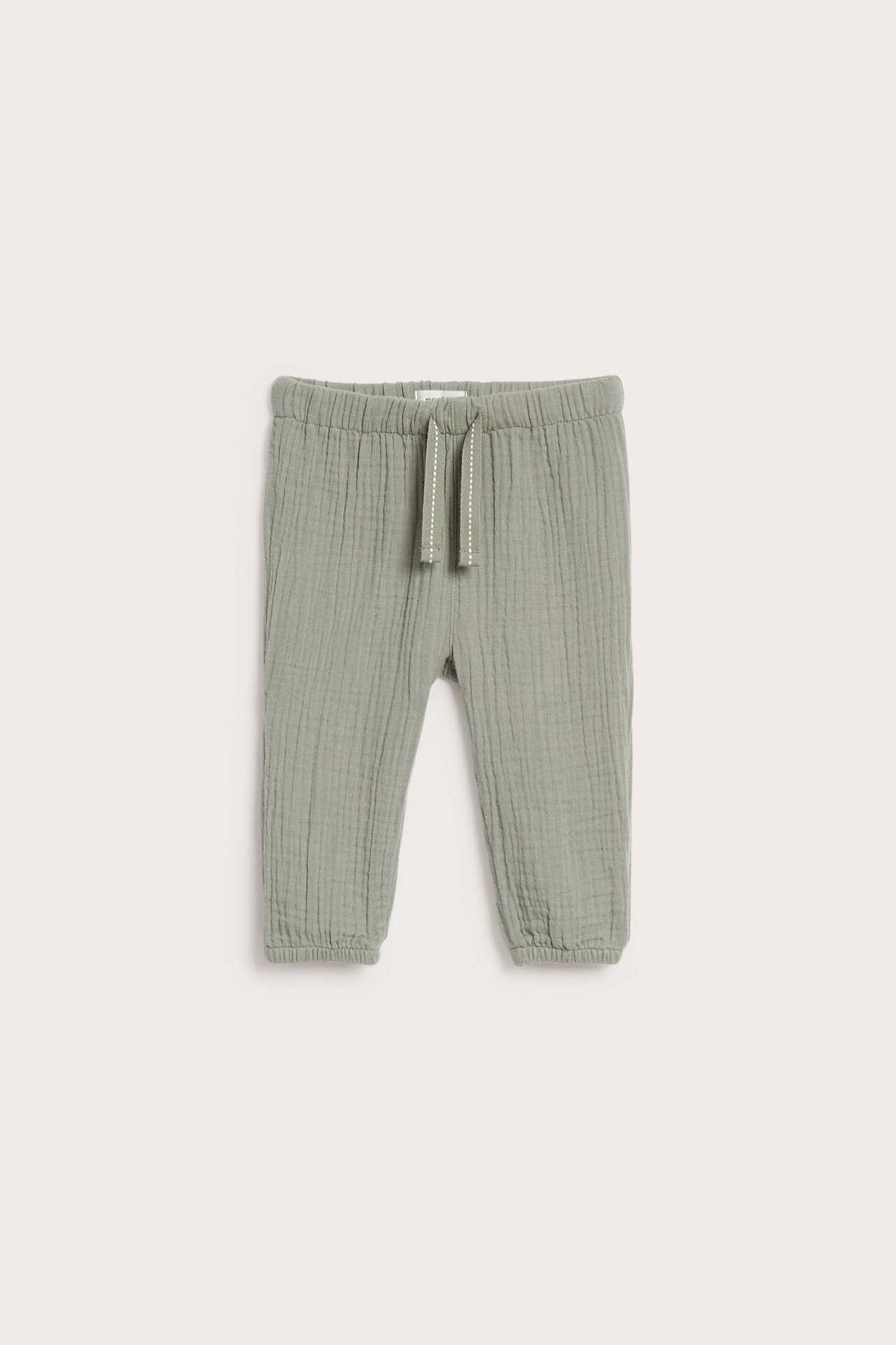 Edestä kuvatut tummanvihreät lasten musliinihousut, joissa joustovyötärö, kiristysnyöri ja joustavat lahkeensuut.